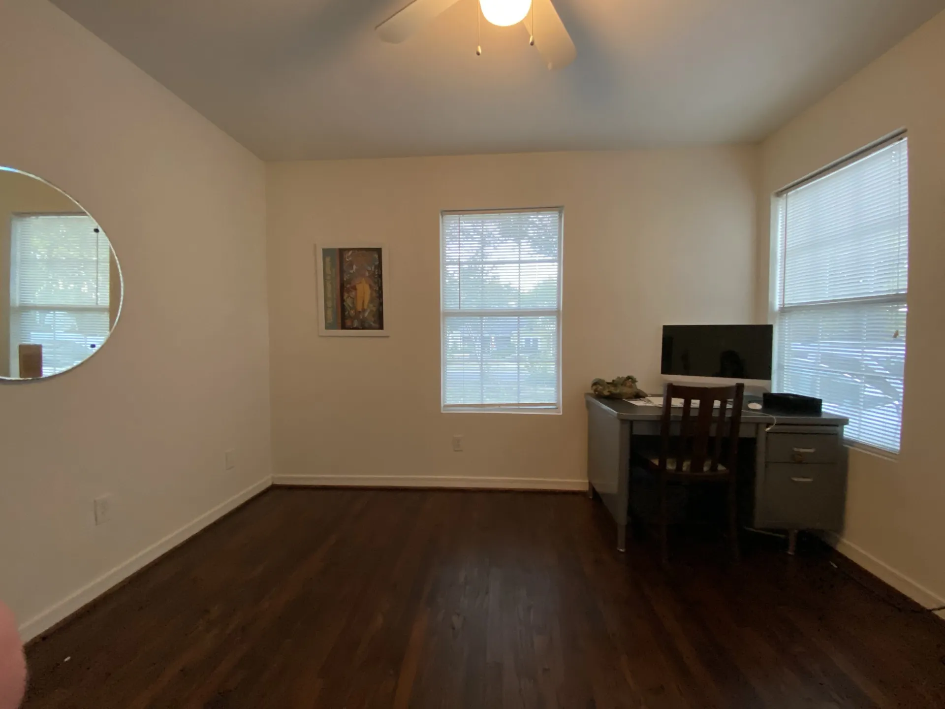 Hardwood flooring complemented by multiple windows with blinds, a ceiling fan with integrated lighting, and neutral wall tones