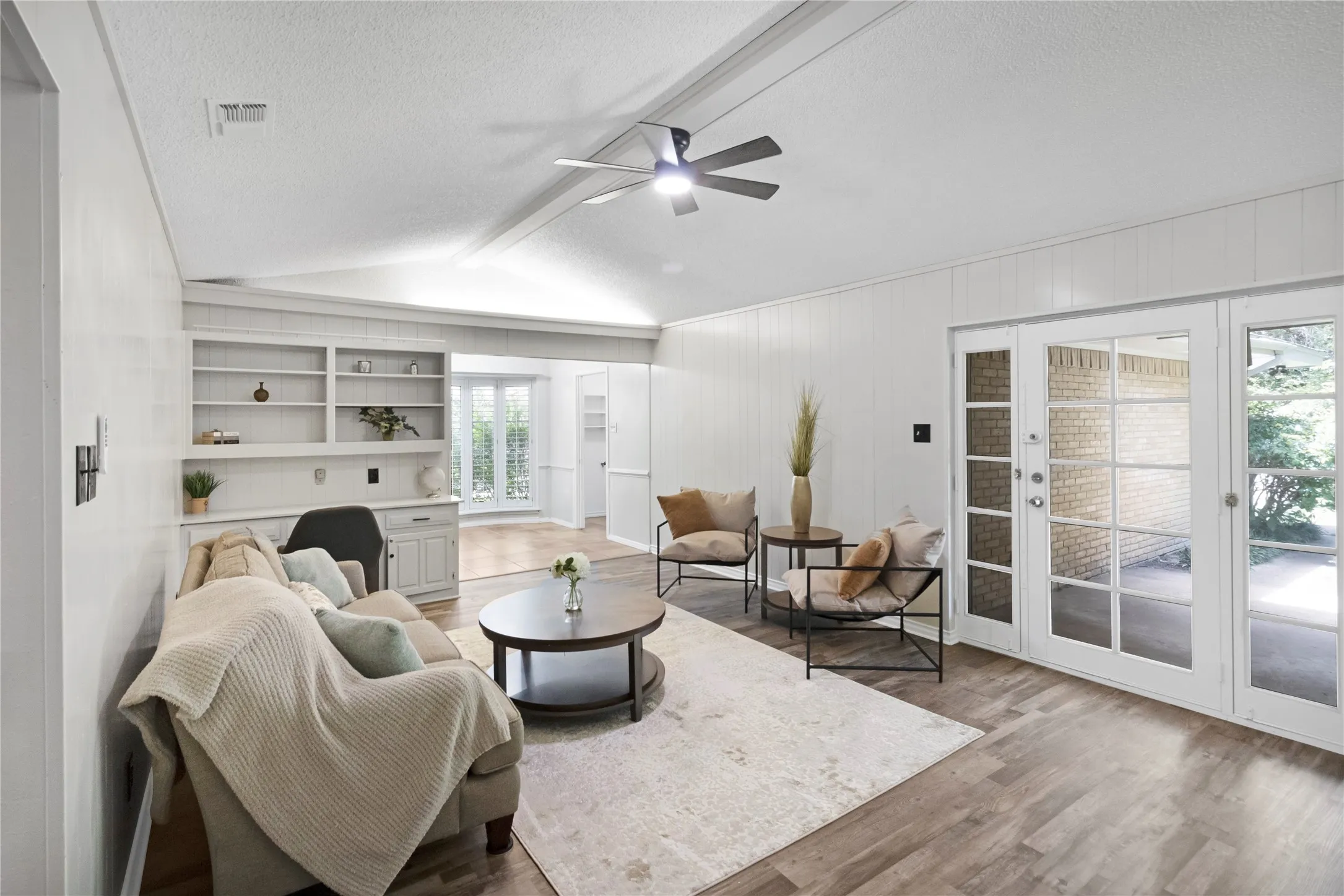 Vaulted ceiling with exposed beams, wood-finish flooring, built-in shelving and cabinetry, and multiple glass-paned doors