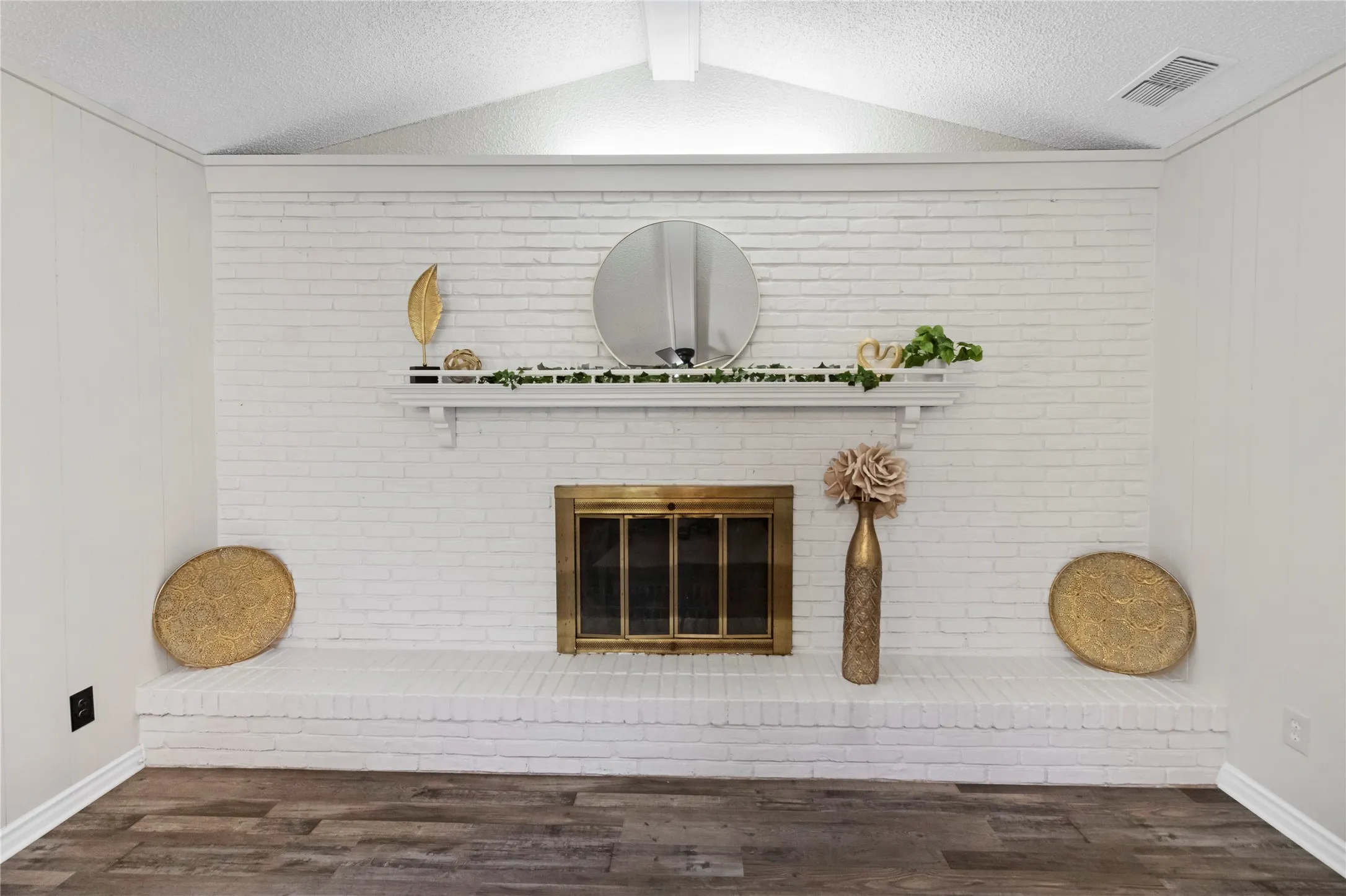 White-painted brick fireplace with a brass firebox, mantel, and wood-finish flooring