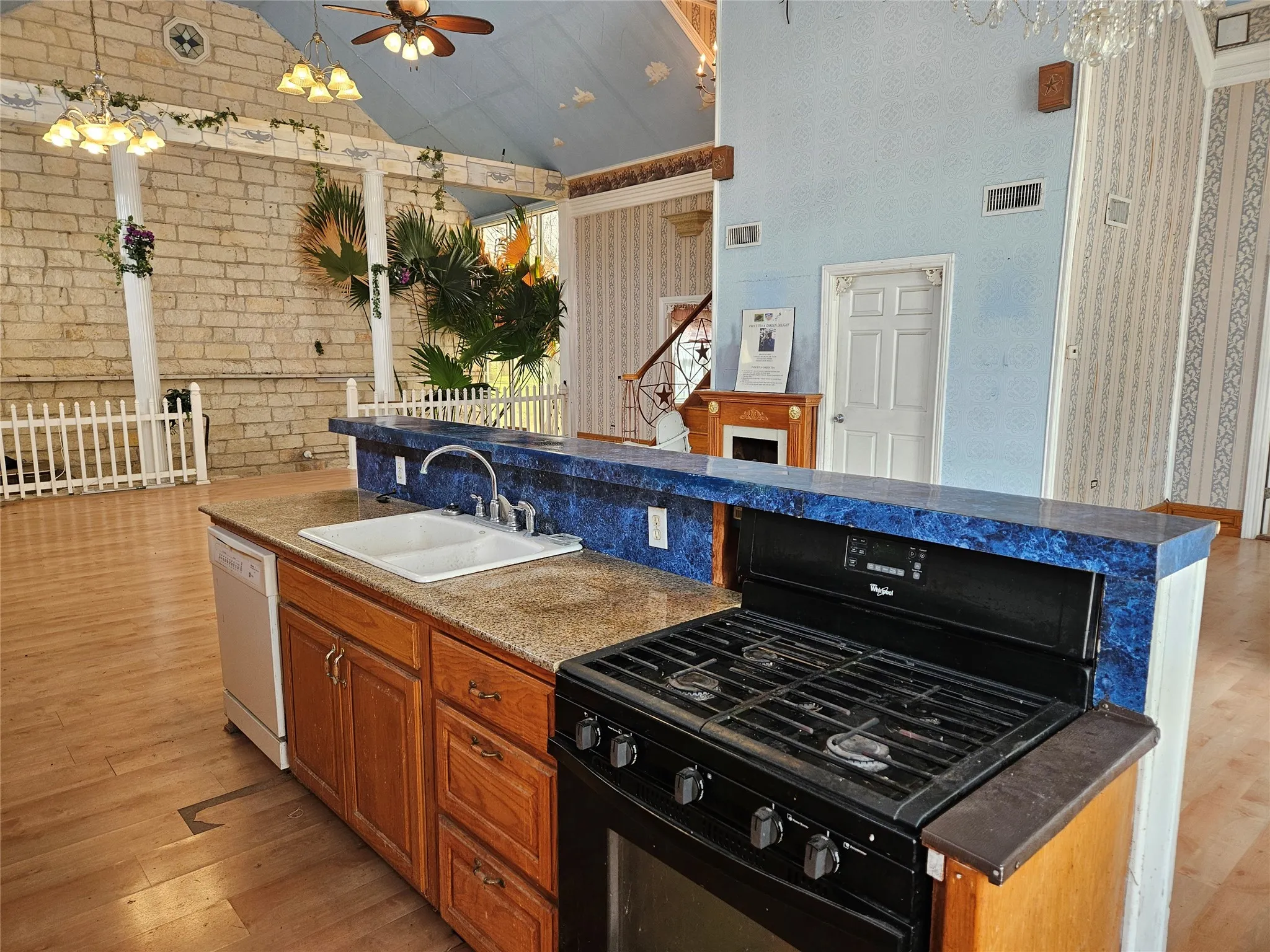 Kitchen featuring black gas range, wood finish cabinets, light wood-style floors, brick wall, and a high ceiling