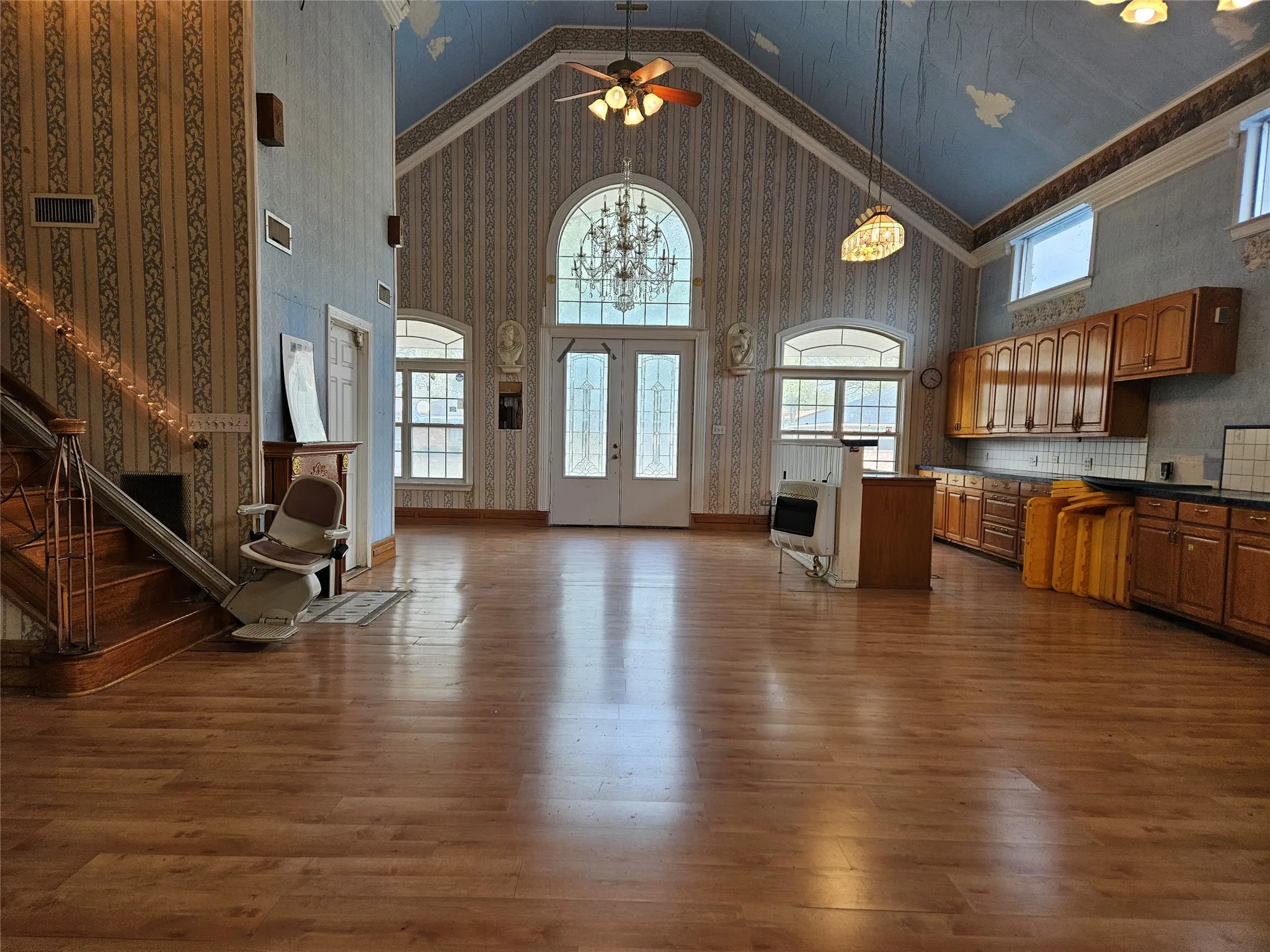 Living room featuring a high ceiling, wallpapered walls, dark wood-style floors, a ceiling fan, and heating unit