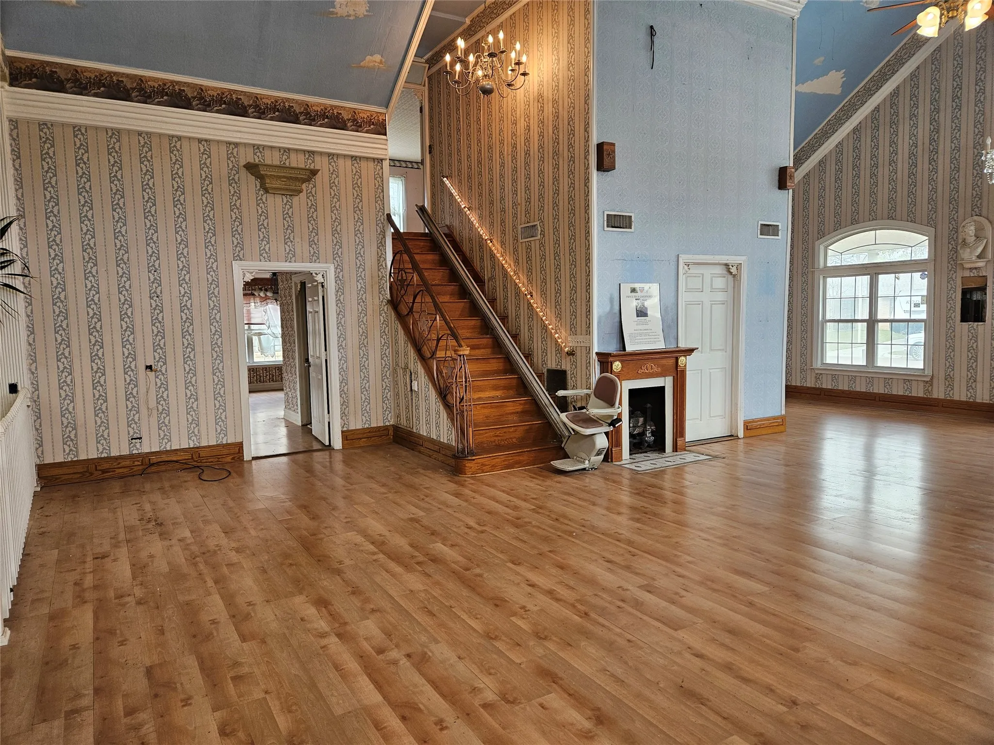 Unfurnished living room featuring wallpapered walls, a high ceiling, crown molding, wood finished floors, and a fireplace with flush hearth