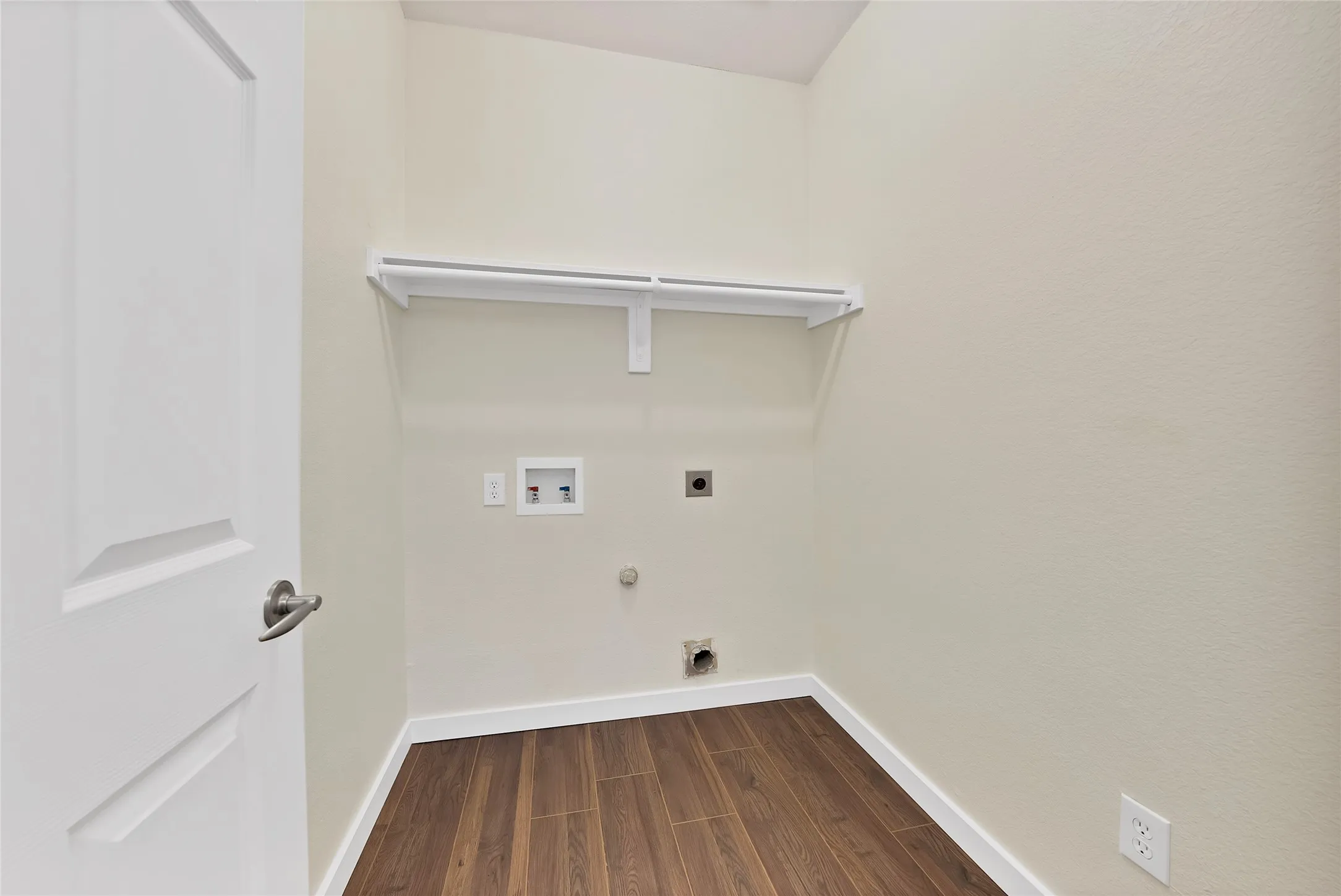 Laundry area featuring wood-finish flooring, white trim, and a built-in shelf