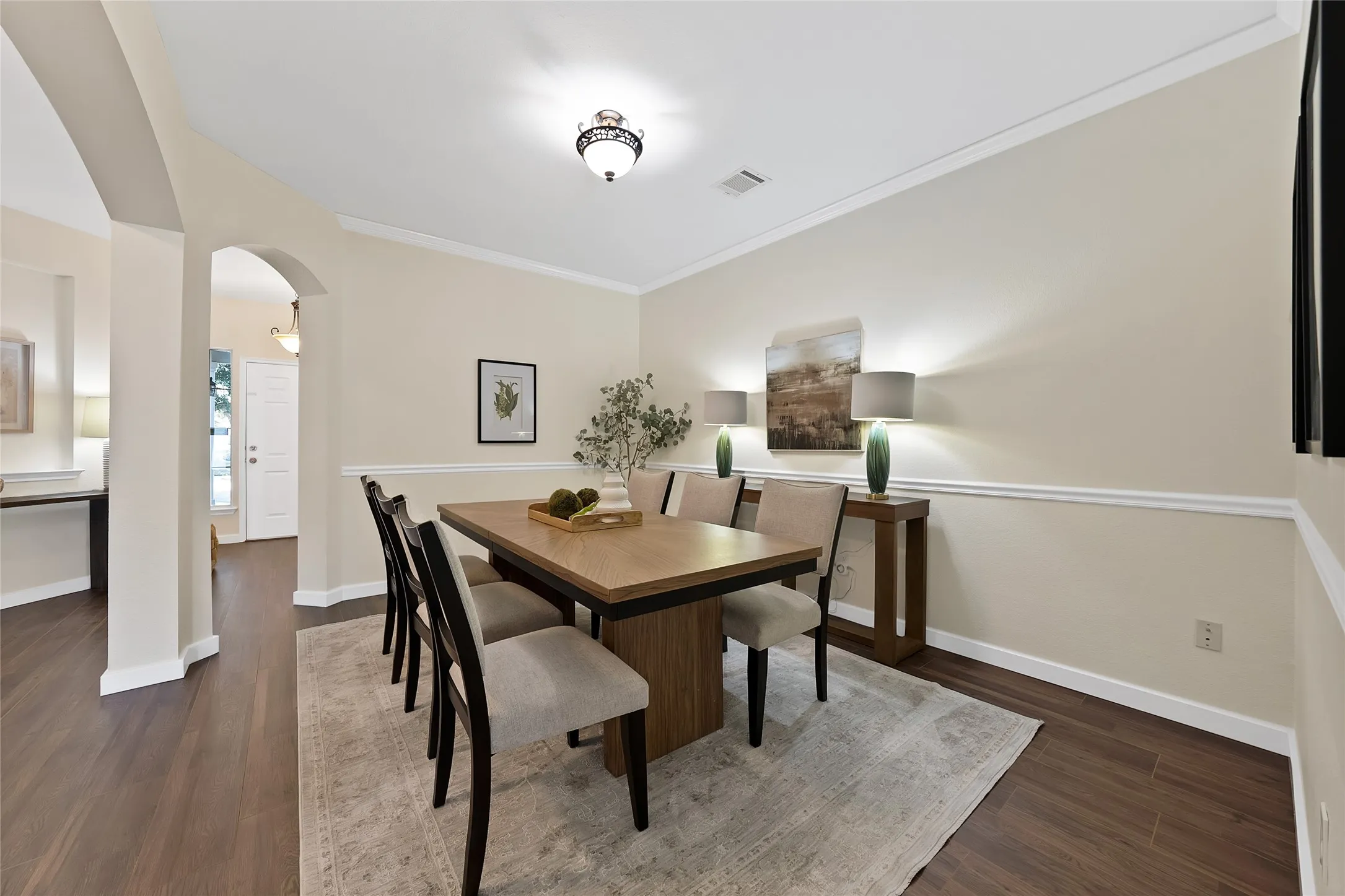Arched entryway with crown molding, wood-finish flooring, and a decorative ceiling light fixture