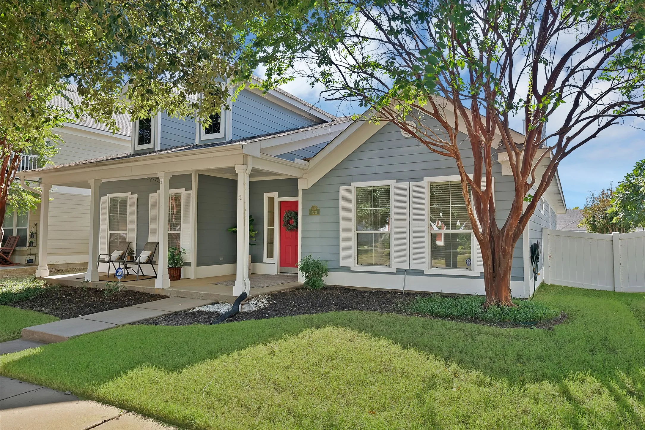 Siding exterior with white trim, covered front porch, red entry door, white window shutters, and a white privacy fence