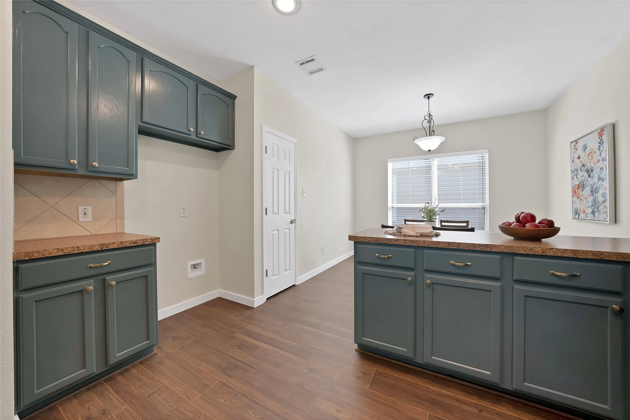 Kitchen featuring wood-finish flooring, dark-toned cabinetry, light-toned countertops, and a tiled backsplash