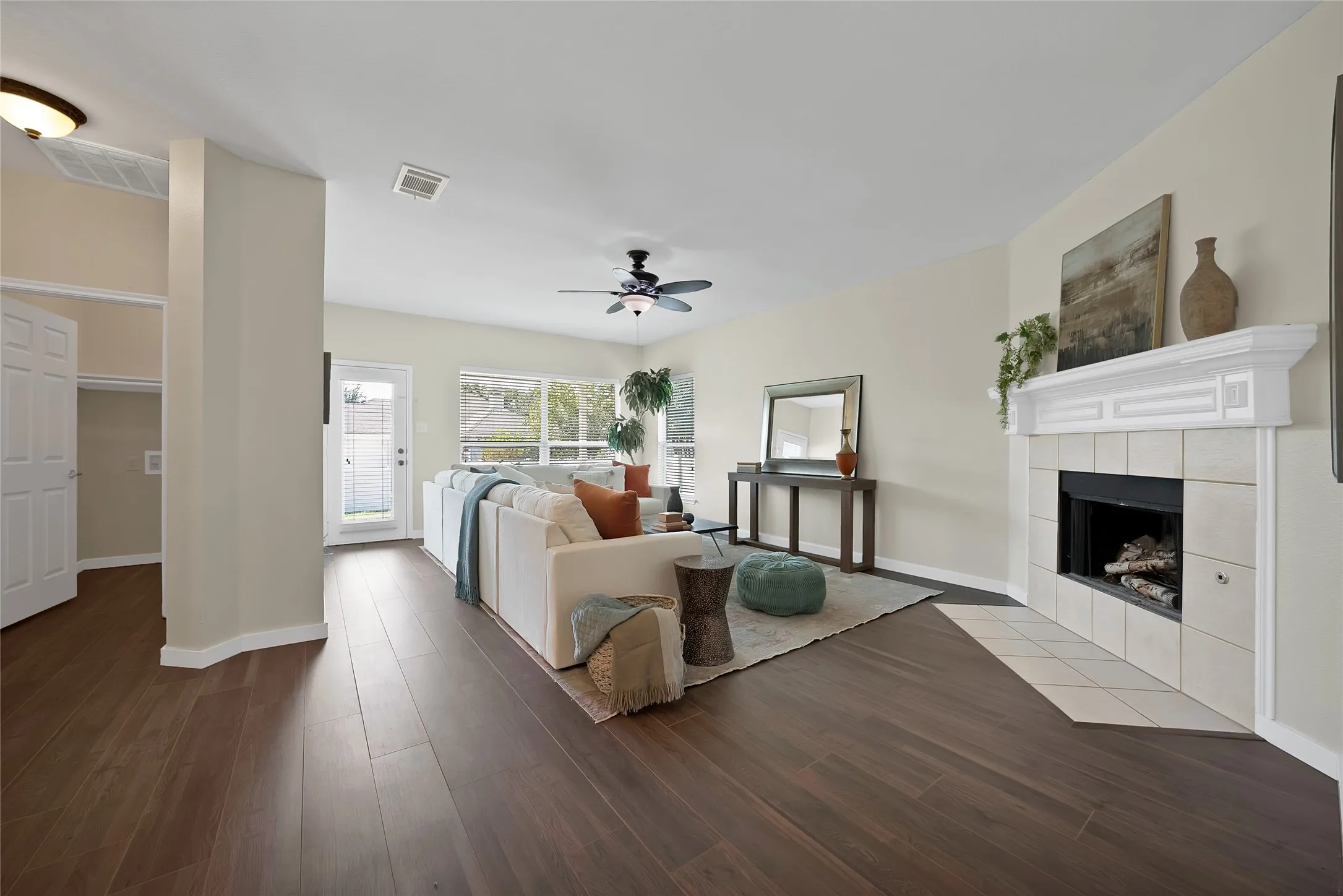 Spacious living area featuring wood-finish flooring, a tiled fireplace with a white mantel, and a ceiling fan
