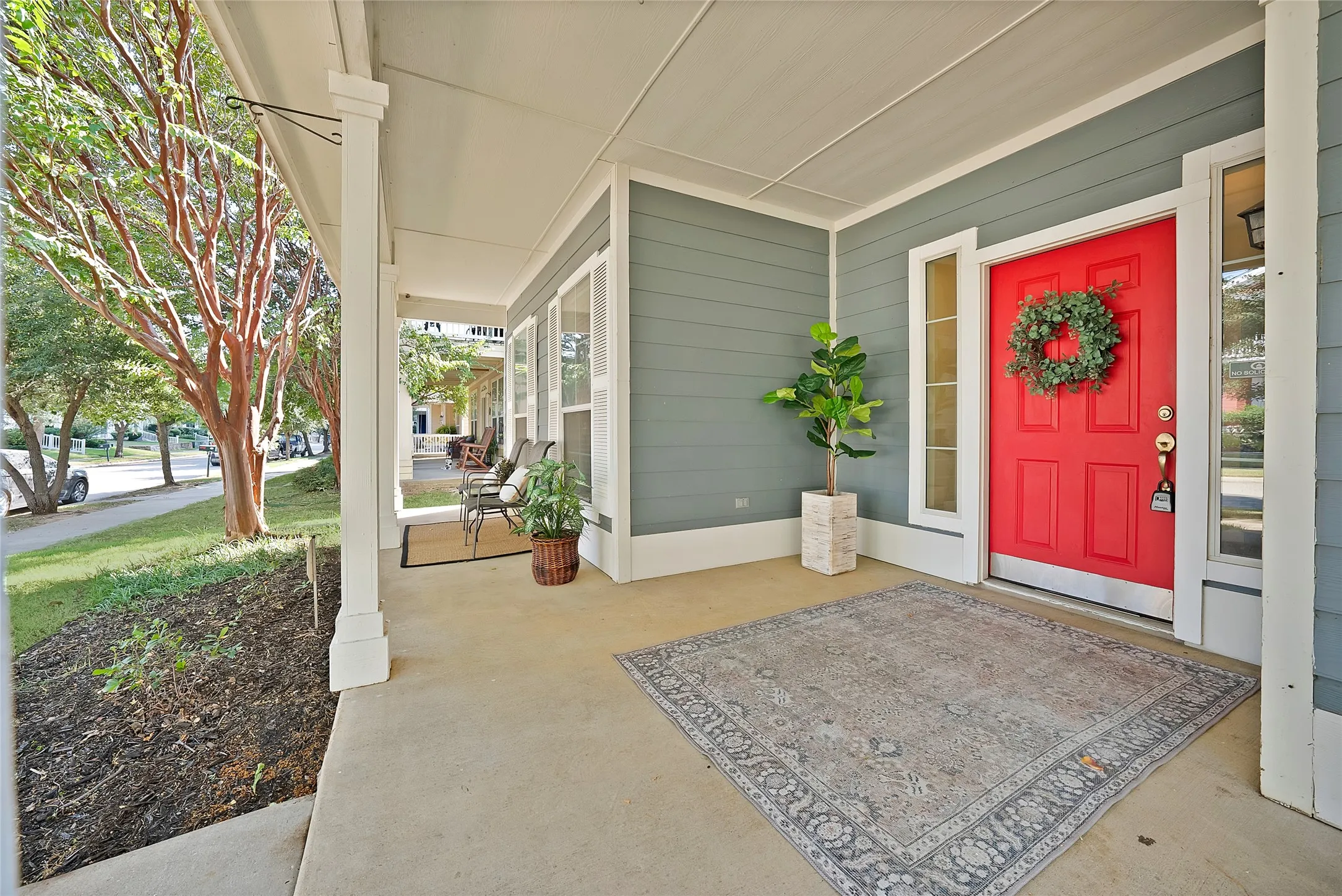 Concrete front porch with white columns, horizontal siding, and a red entry door with sidelights