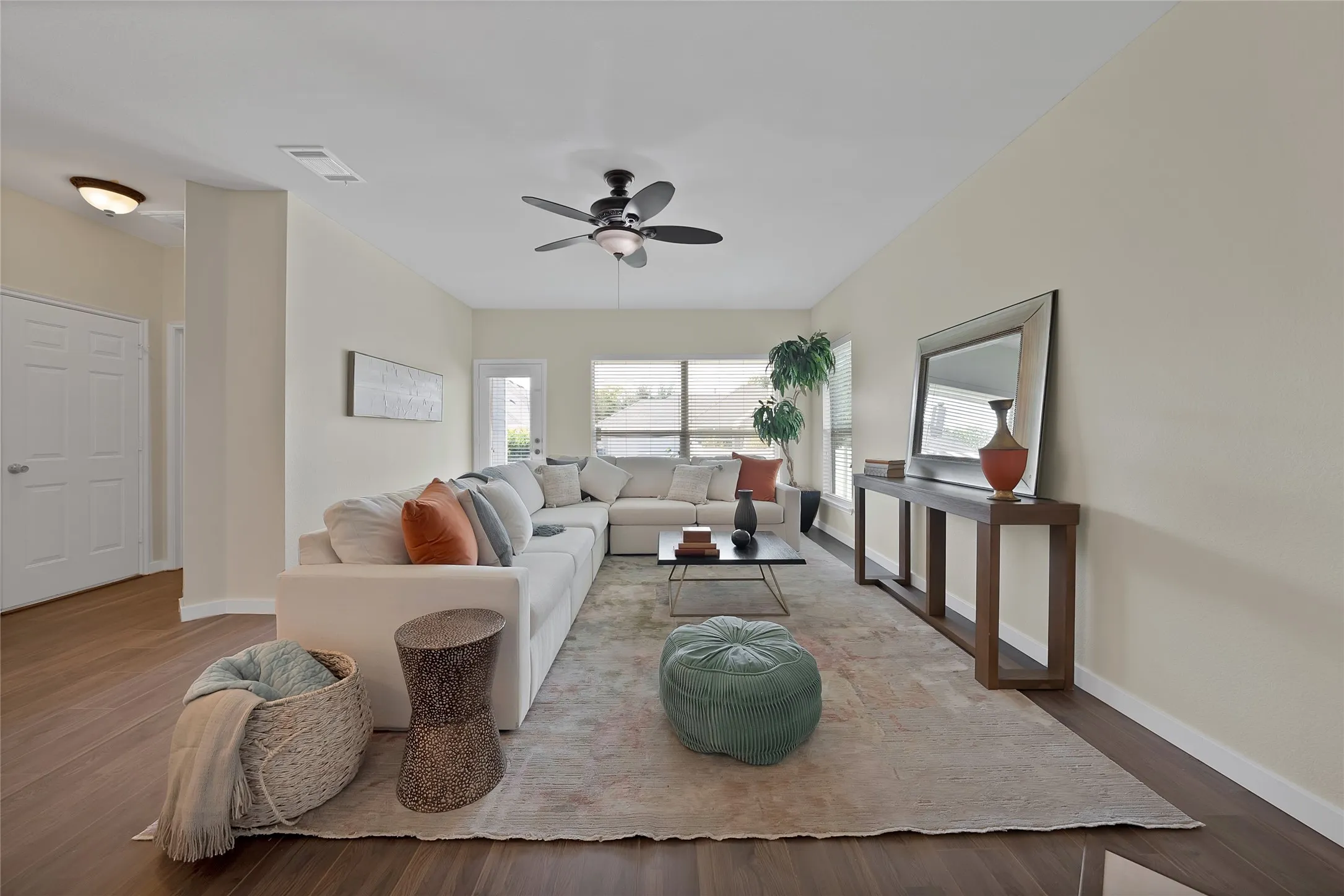 Spacious living area featuring wood-finish flooring, a ceiling fan, and ample natural light from multiple windows