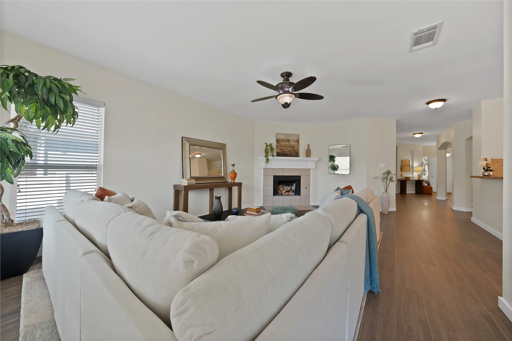 Spacious living area featuring wood-finish flooring, a ceiling fan, and a fireplace with a white mantel