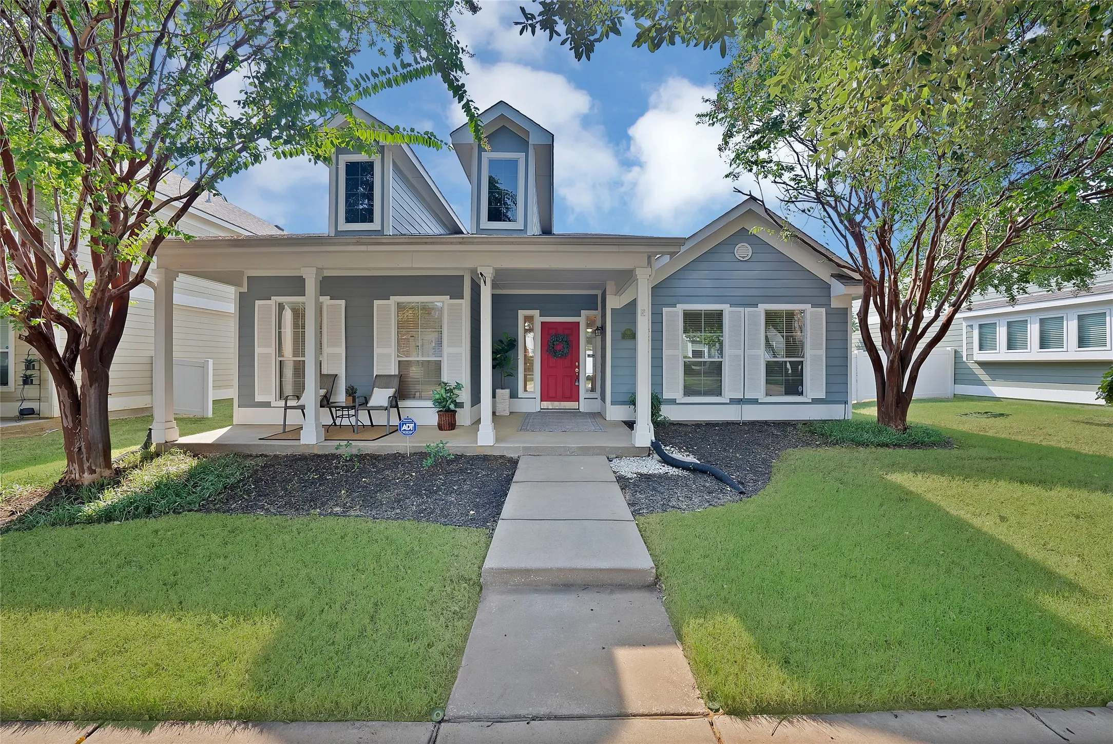 Exterior featuring a covered front porch, dormer windows, and a red entry door