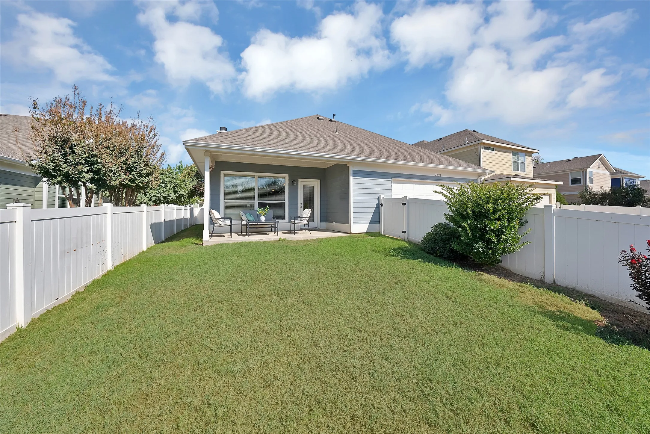 Expansive backyard featuring a manicured lawn, white privacy fencing, and a concrete patio