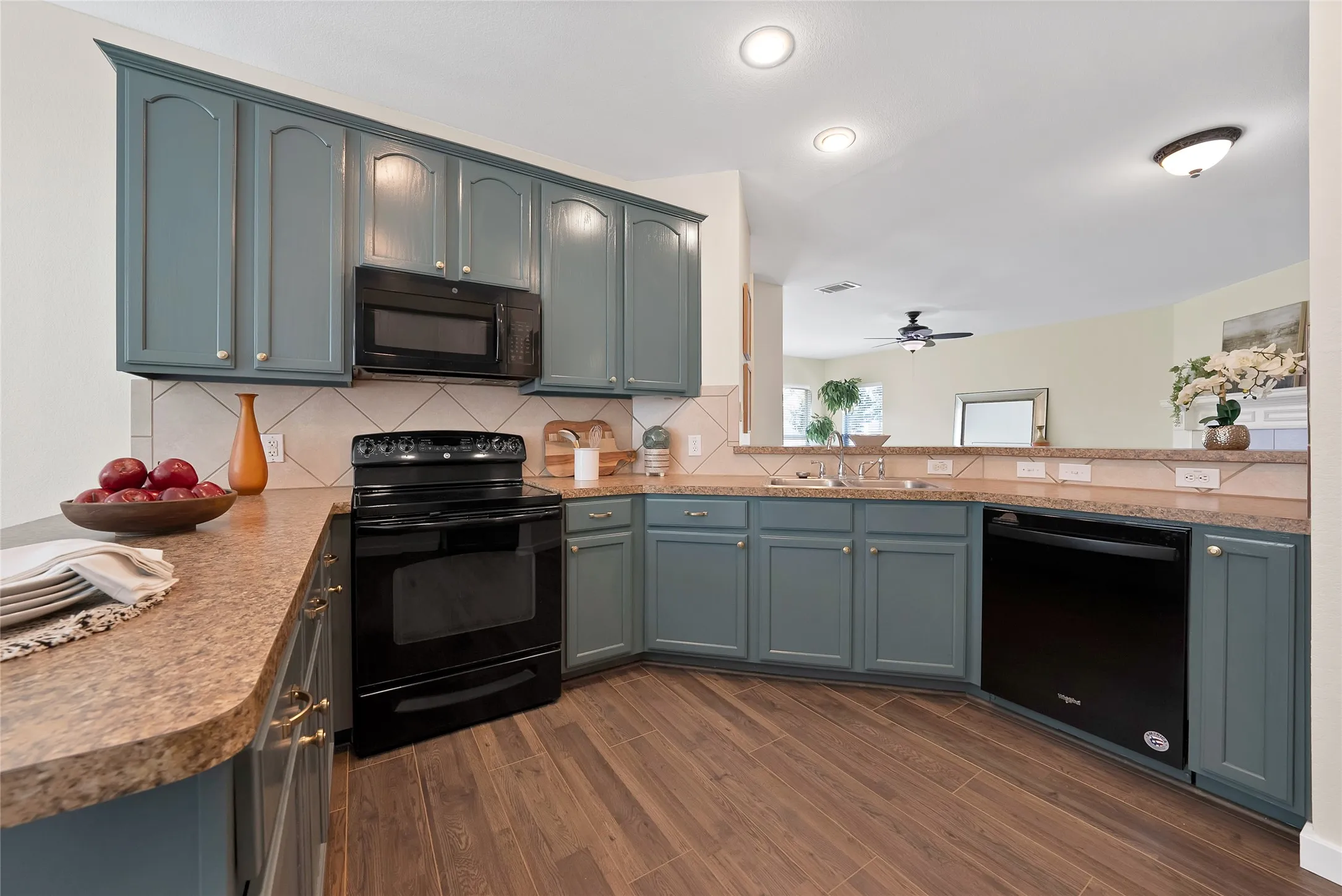 Curved countertops, built-in microwave, black appliances, tile backsplash, and wood-finish flooring