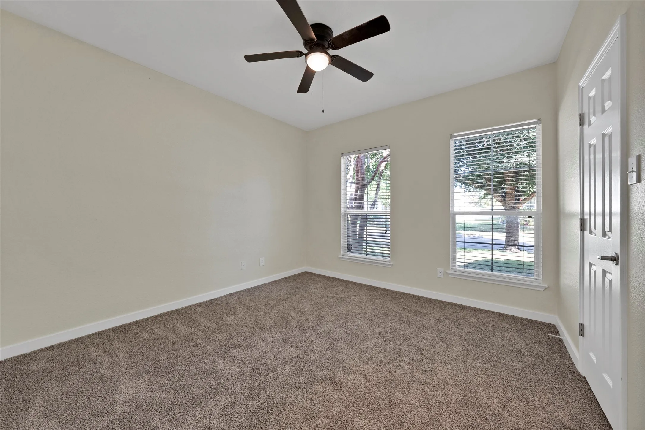 Expansive room featuring neutral wall finishes, carpeted flooring, two windows with blinds, a ceiling fan with integrated lighting, and a paneled door