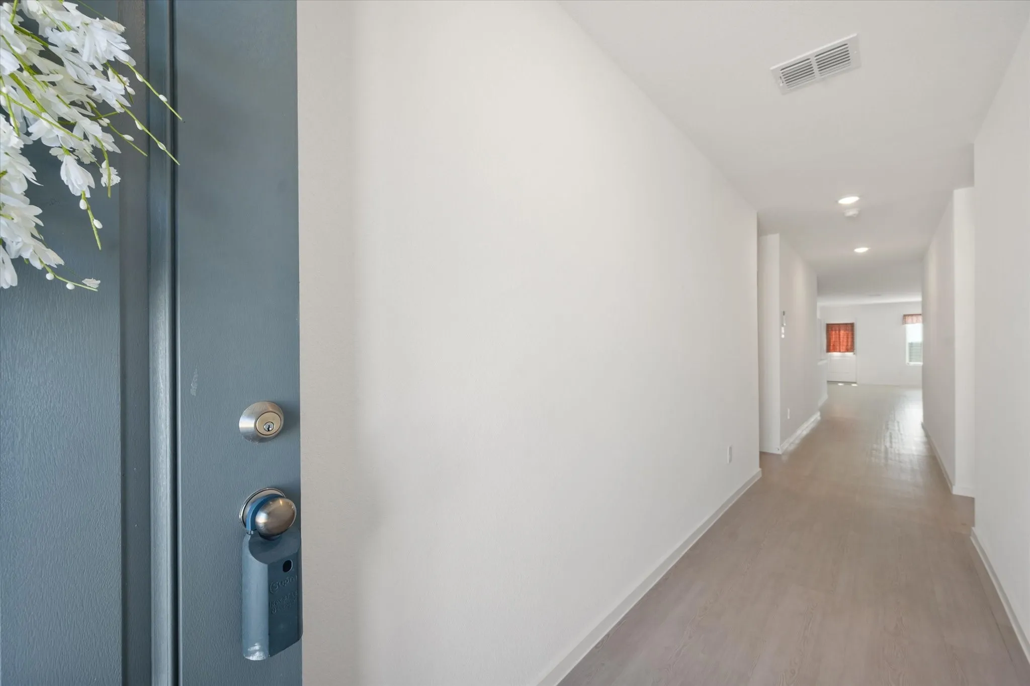 Light-toned wood-finish flooring extending through a hallway with white walls and recessed ceiling lighting