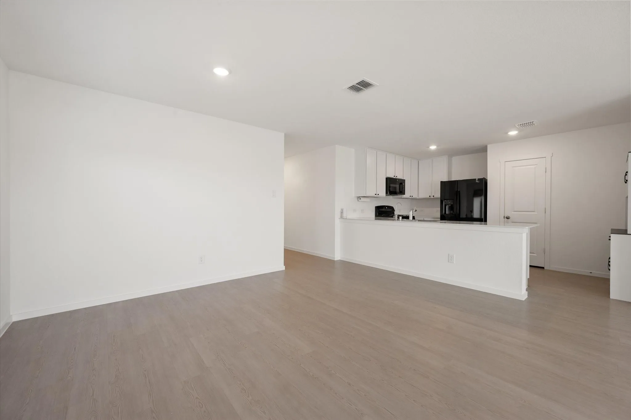 Open-concept living area featuring wood-finish flooring, recessed lighting, and a kitchen with white cabinetry, a kitchen island, and black appliances