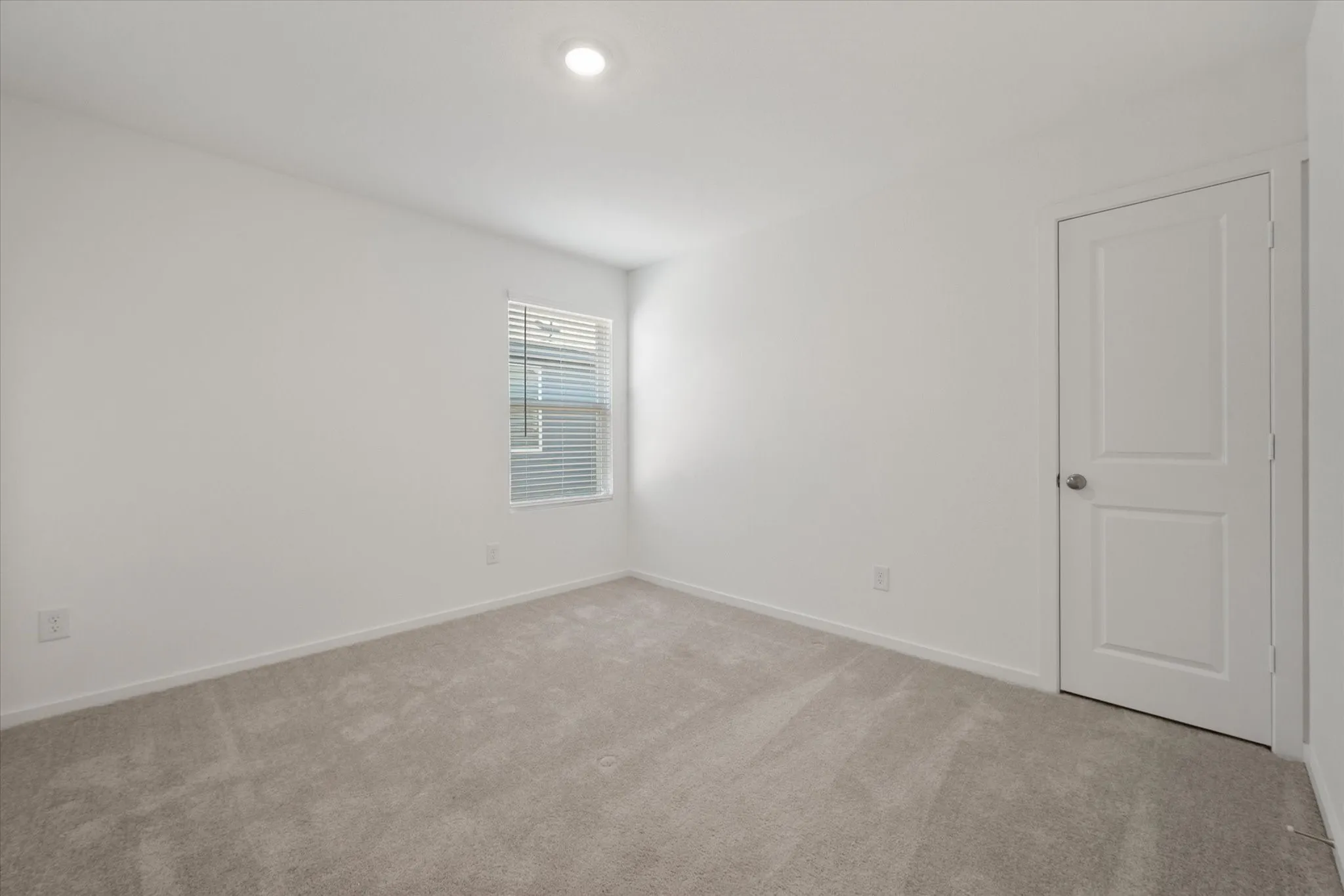 Neutral wall paint, light-colored carpeting, recessed ceiling light, window with blinds, and a two-panel interior door