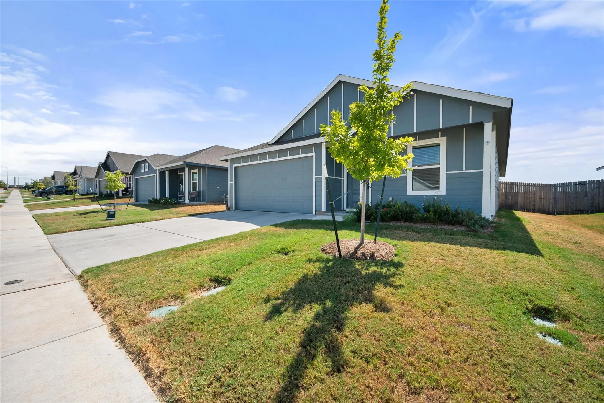 Contemporary exterior siding in a blue-gray finish, attached garage with a matching door, concrete driveway, sidewalk, and a wood privacy fence