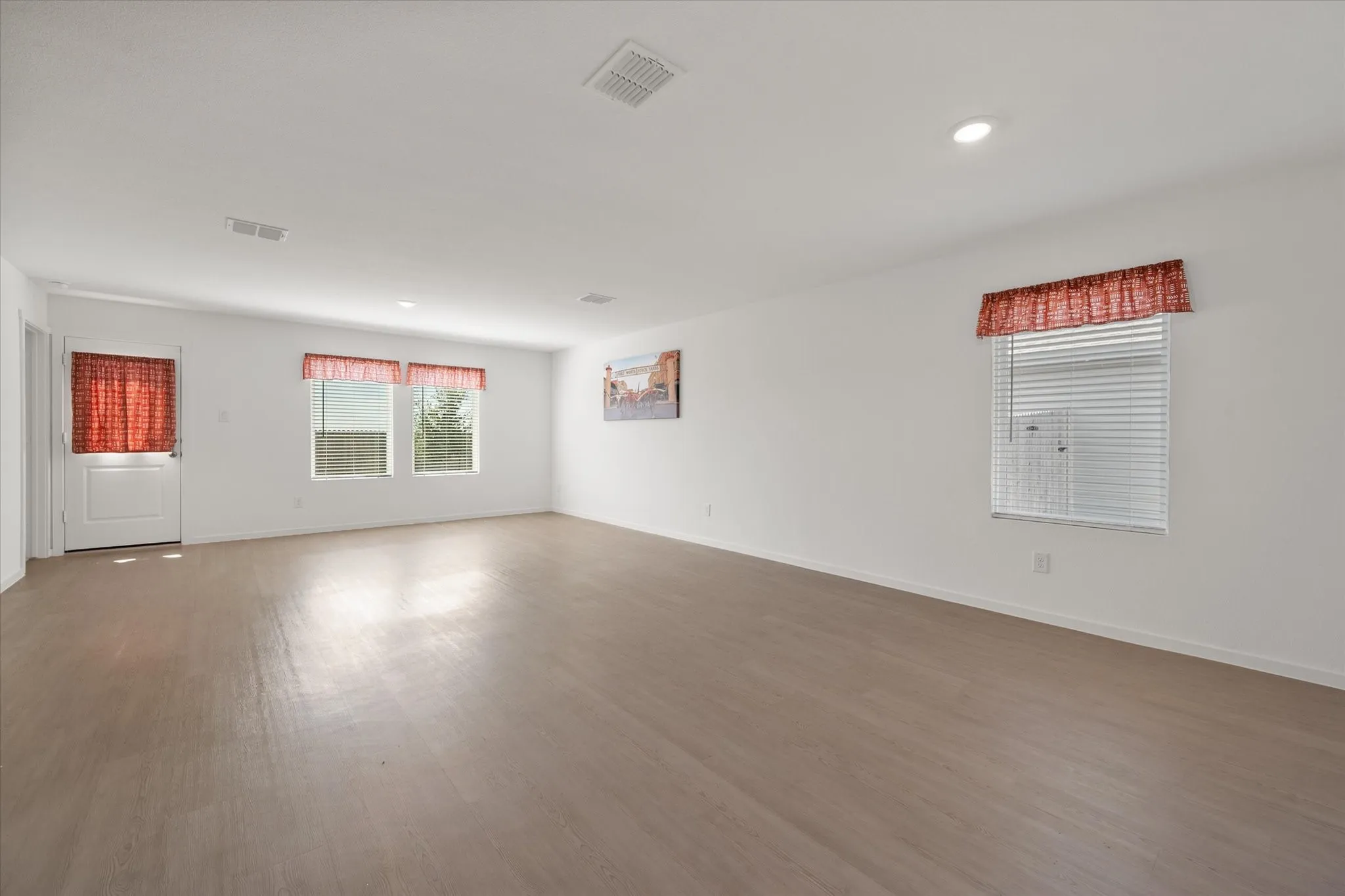 Spacious room with wood-finish flooring, white walls, multiple windows, and recessed lighting