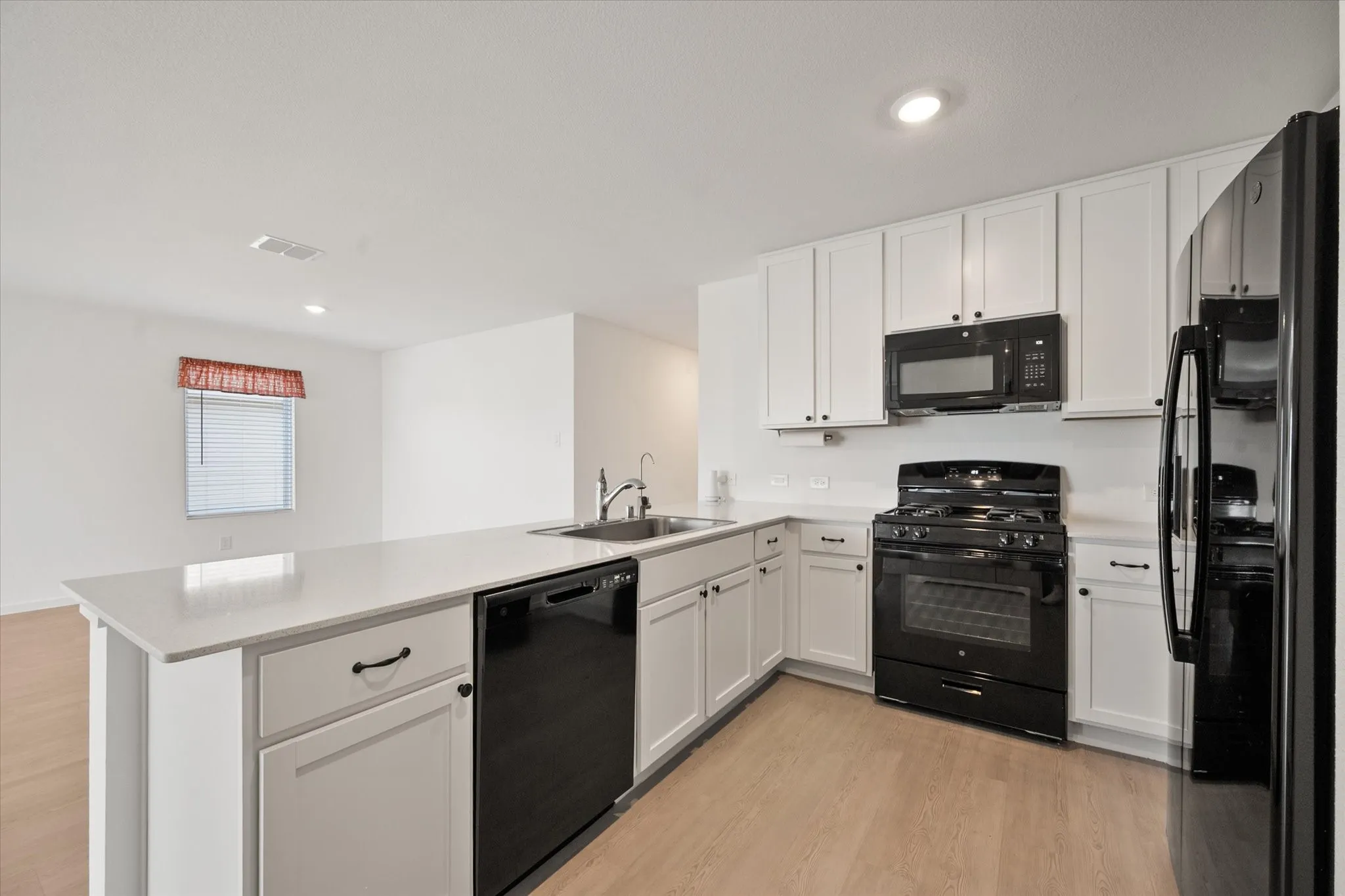 Kitchen featuring white cabinetry, black appliances, a stainless steel sink, light countertops, and wood-finish flooring