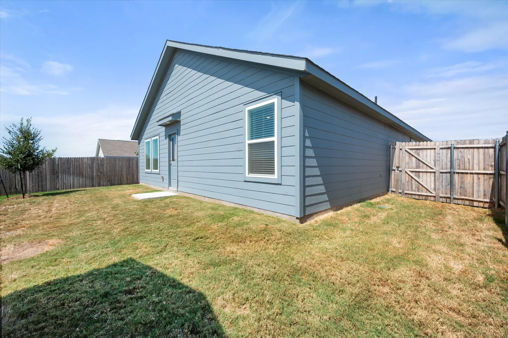 Exterior siding in a blue finish, featuring white window frames and a wooden privacy fence