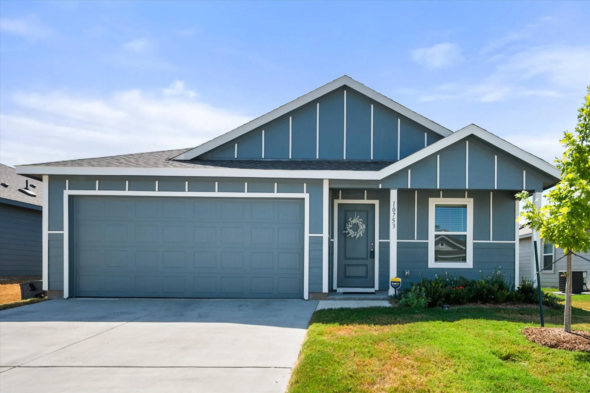 Exterior featuring blue siding, white trim, an attached garage, a paved driveway, and a front entry door with a wreath