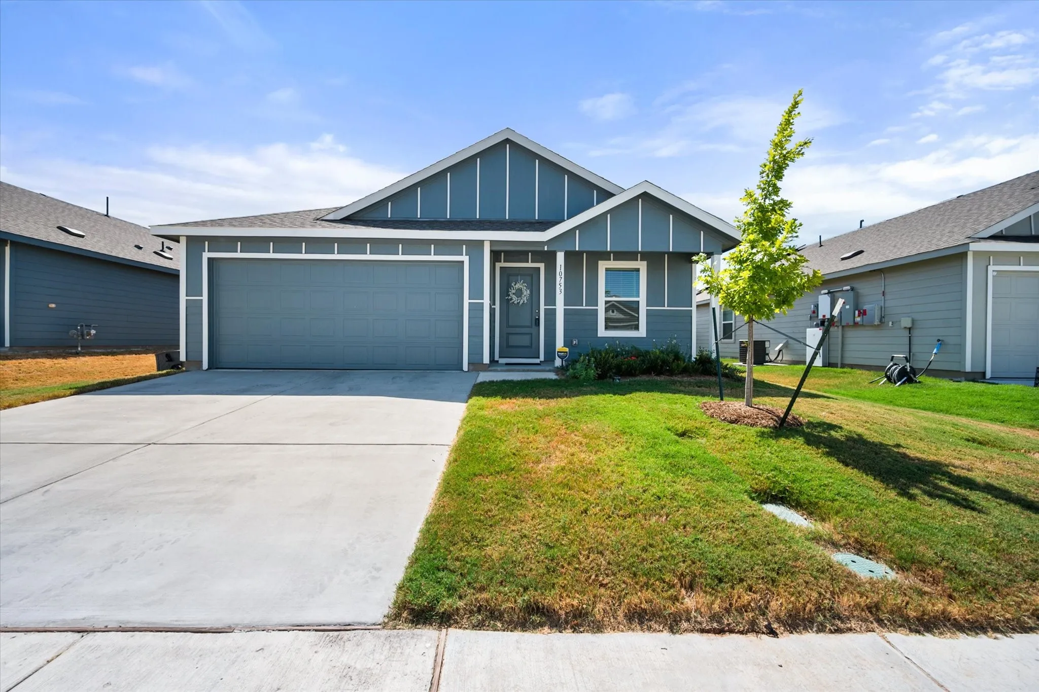 Blue siding exterior with white trim, a concrete driveway, an attached garage, a front door with a window, and a small tree in the front yard