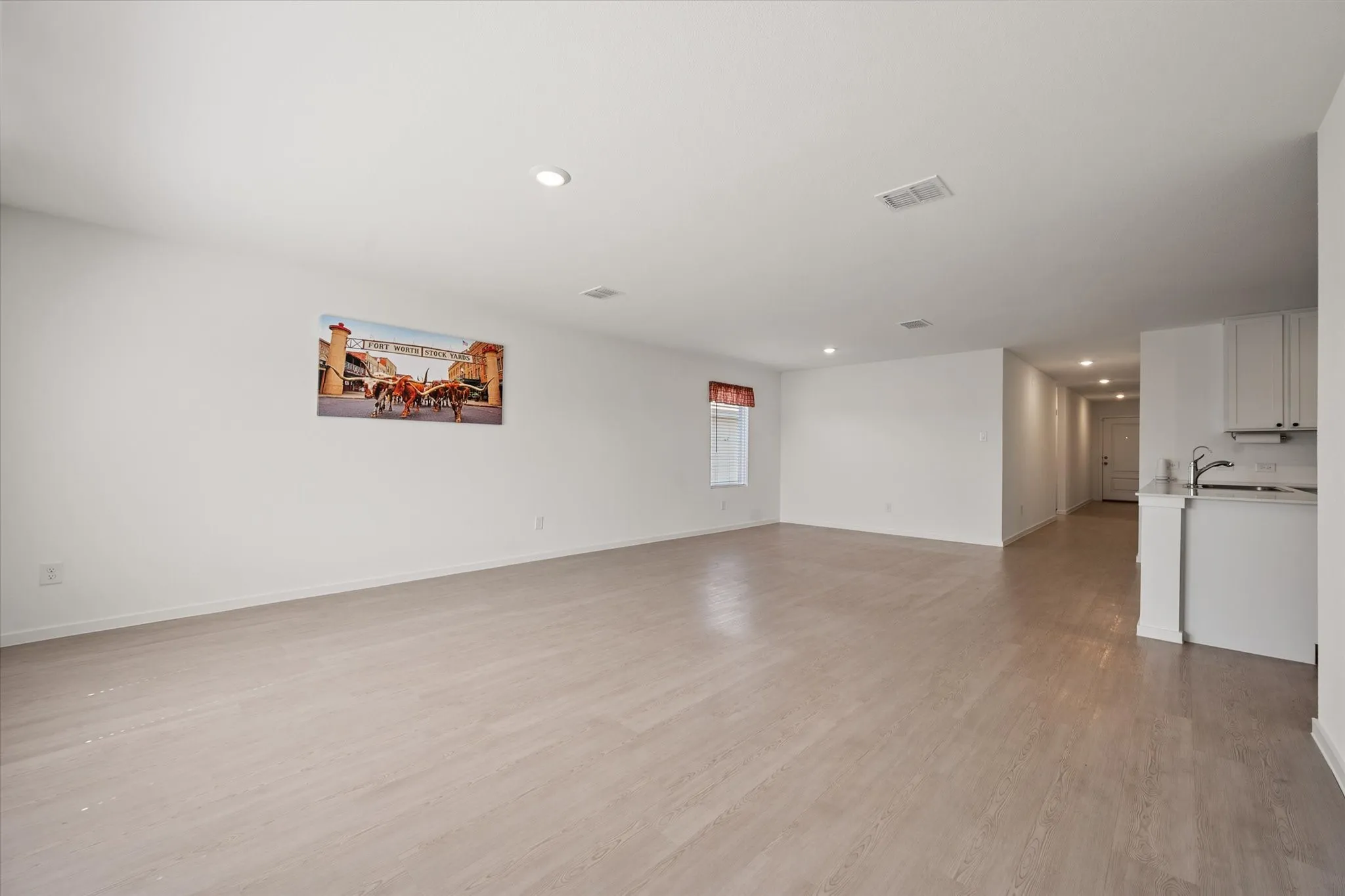 Open-concept living space featuring light wood-finish flooring, recessed lighting, and a kitchen area with white cabinetry and a stainless steel sink