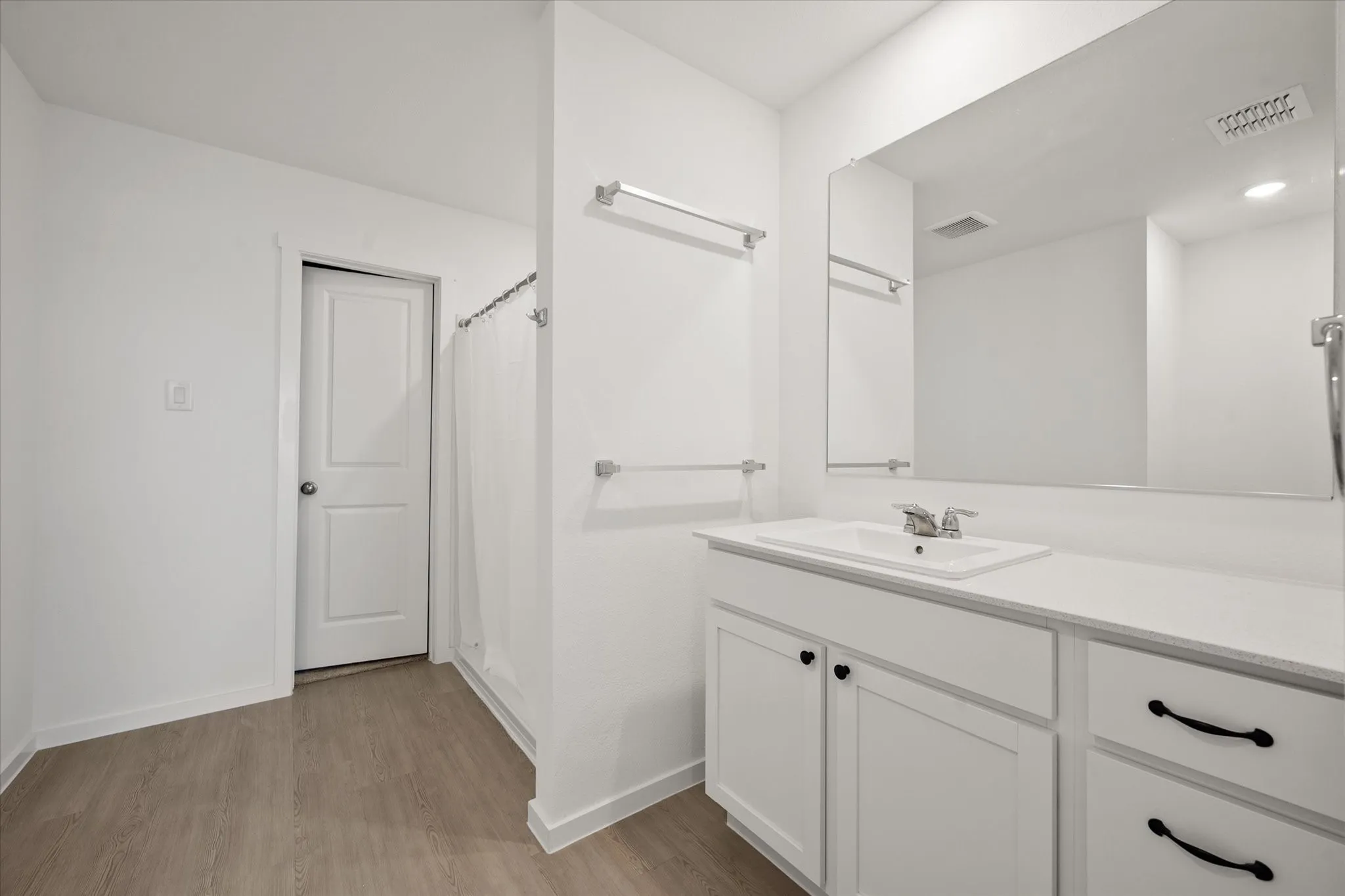Bathroom featuring a vanity with a rectangular sink, a large wall-mounted mirror, wood-finish flooring, and white paneled door