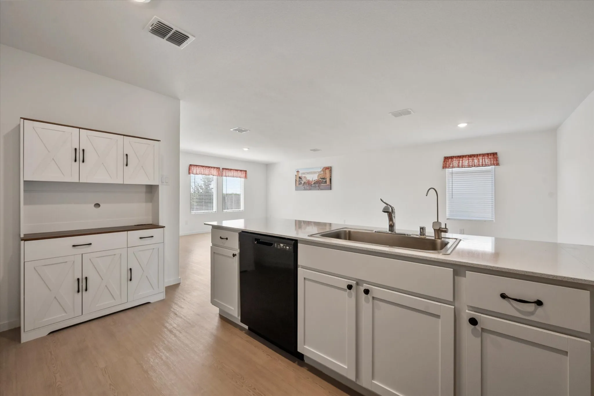 Kitchen featuring an integrated sink, white cabinetry with dark hardware, a built-in dishwasher, and light wood-finish flooring
