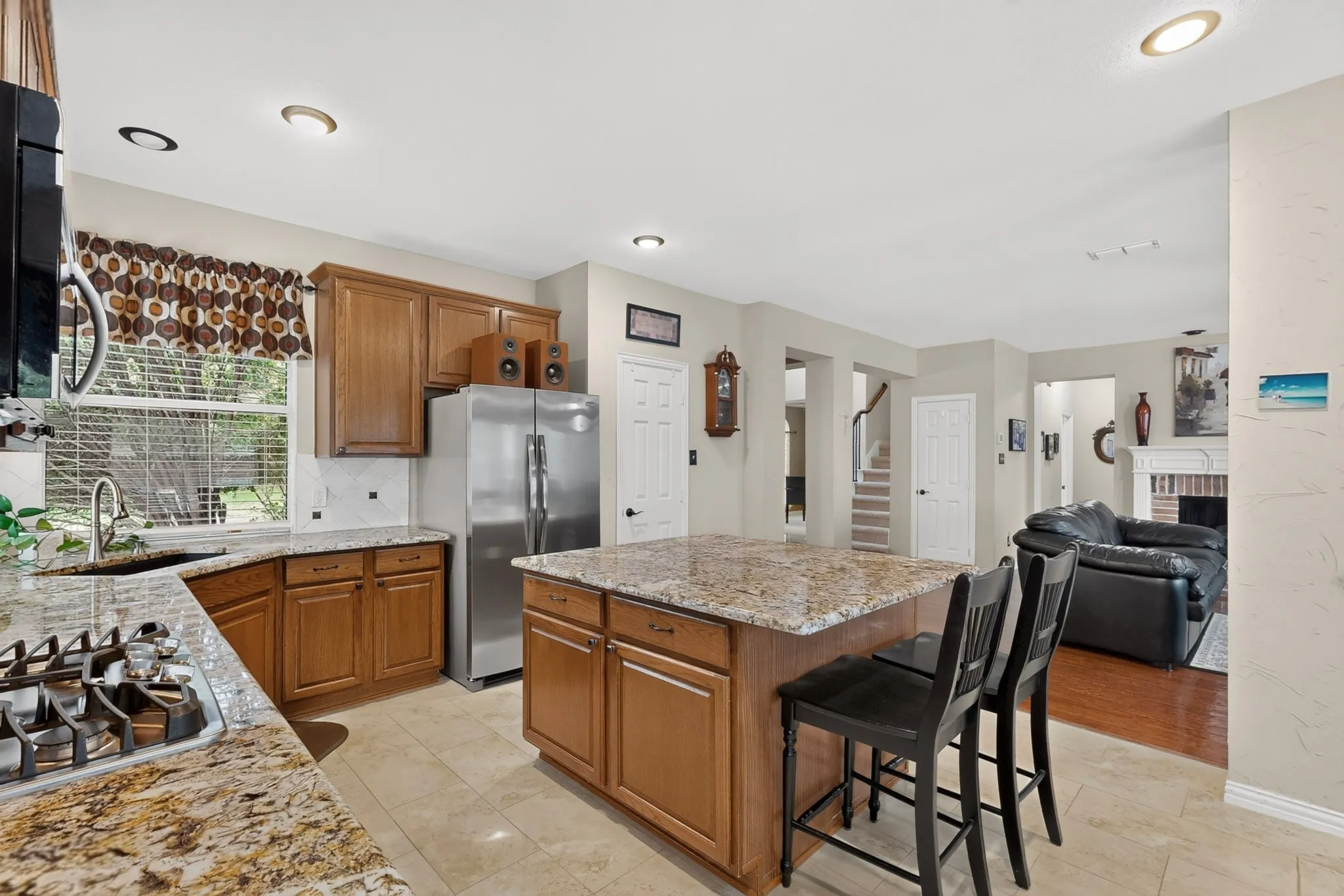 Kitchen with wood cabinetry, granite countertops, tile flooring, stainless steel appliances, and an island with seating