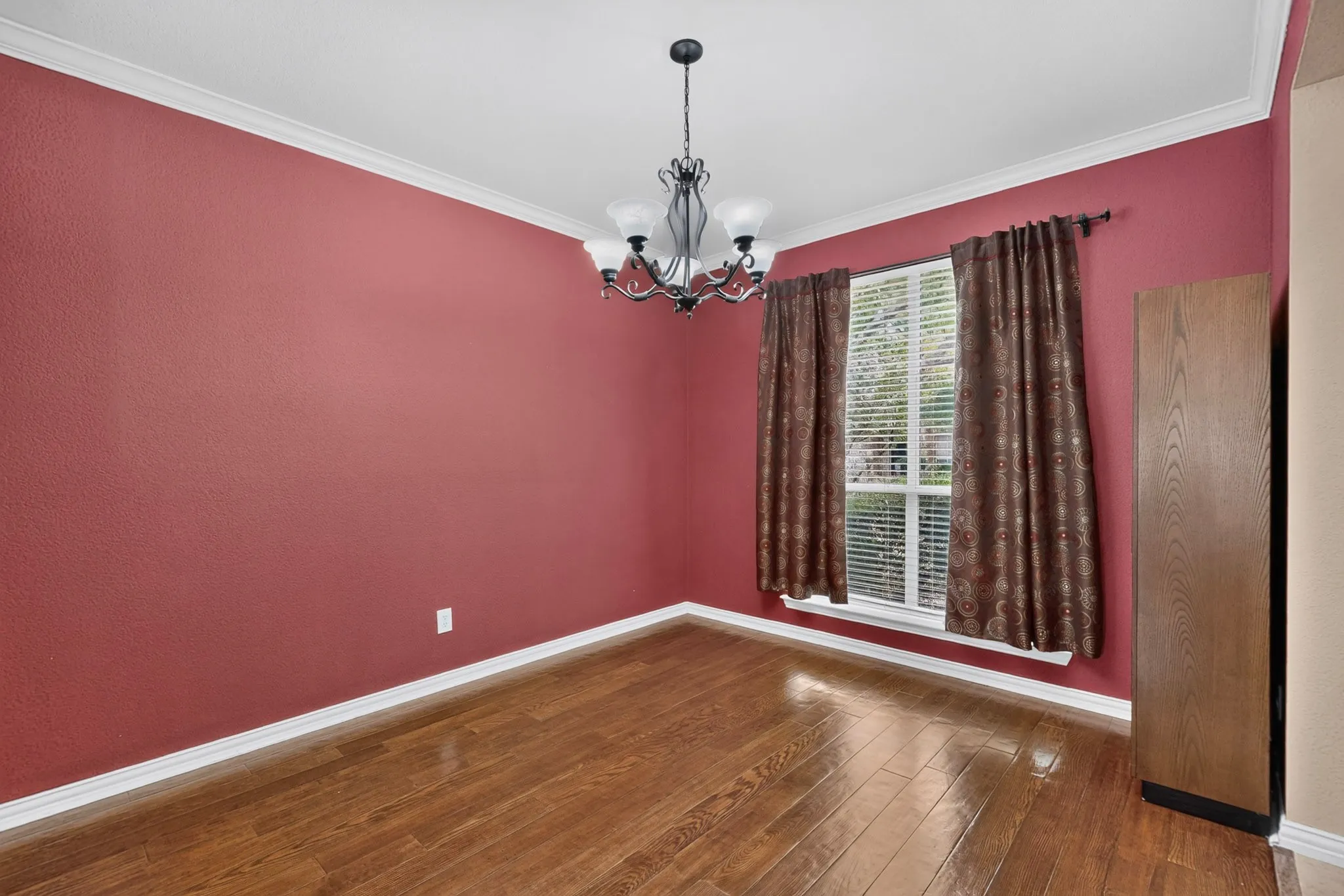 Wood-finish flooring, crown molding, and a chandelier illuminate this interior space