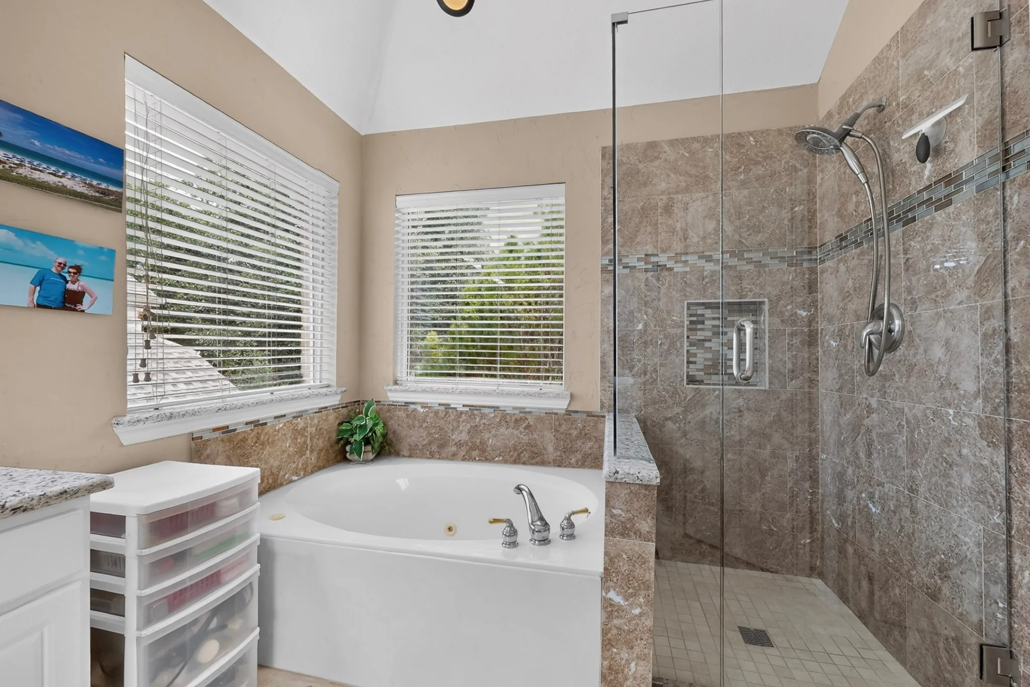 Garden tub with deck-mounted fixtures, separate glass-enclosed shower with tiled walls, vaulted ceiling, and recessed lighting