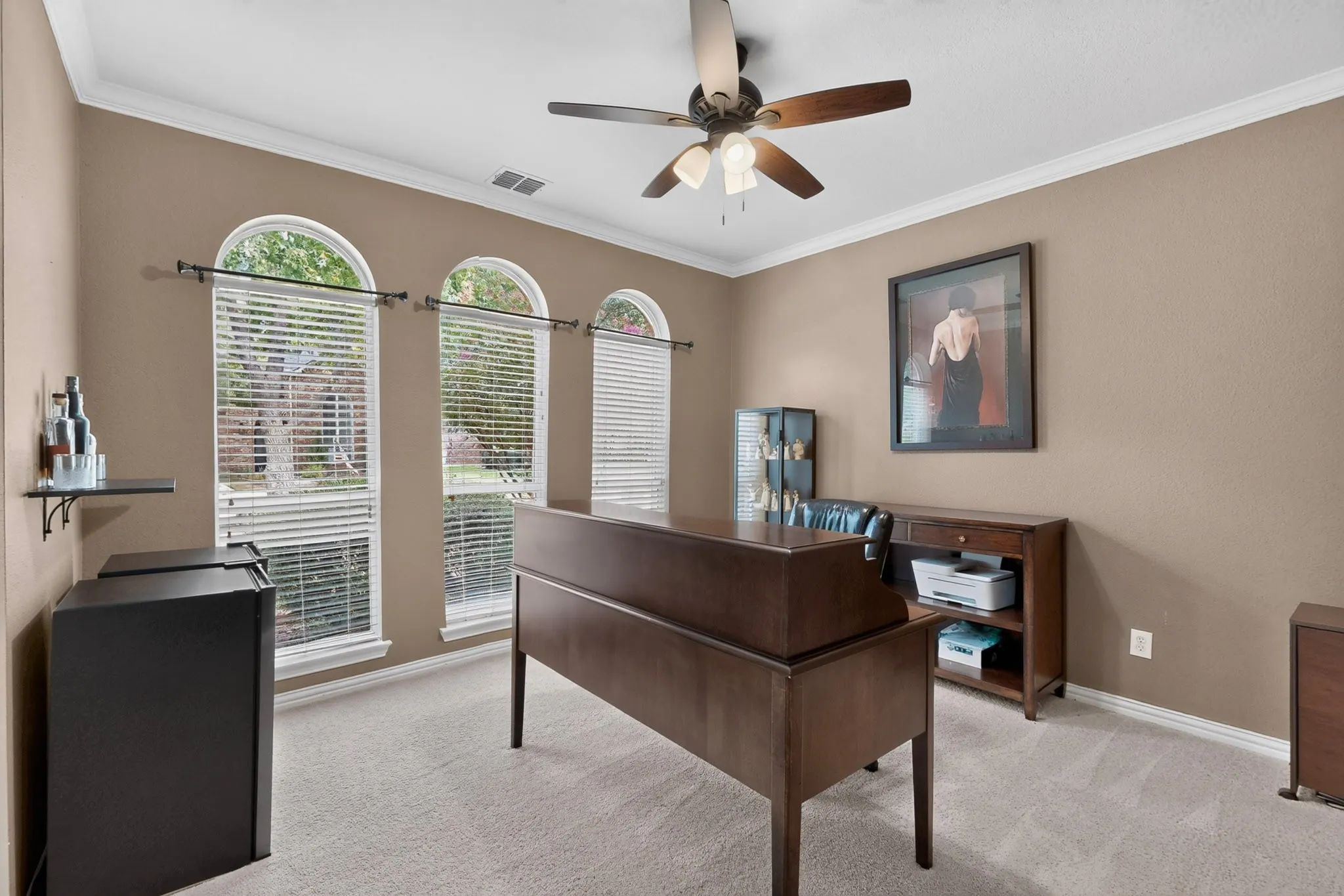Arched windows with blinds, ceiling fan with integrated lighting, neutral wall tones, crown molding, and carpeted flooring