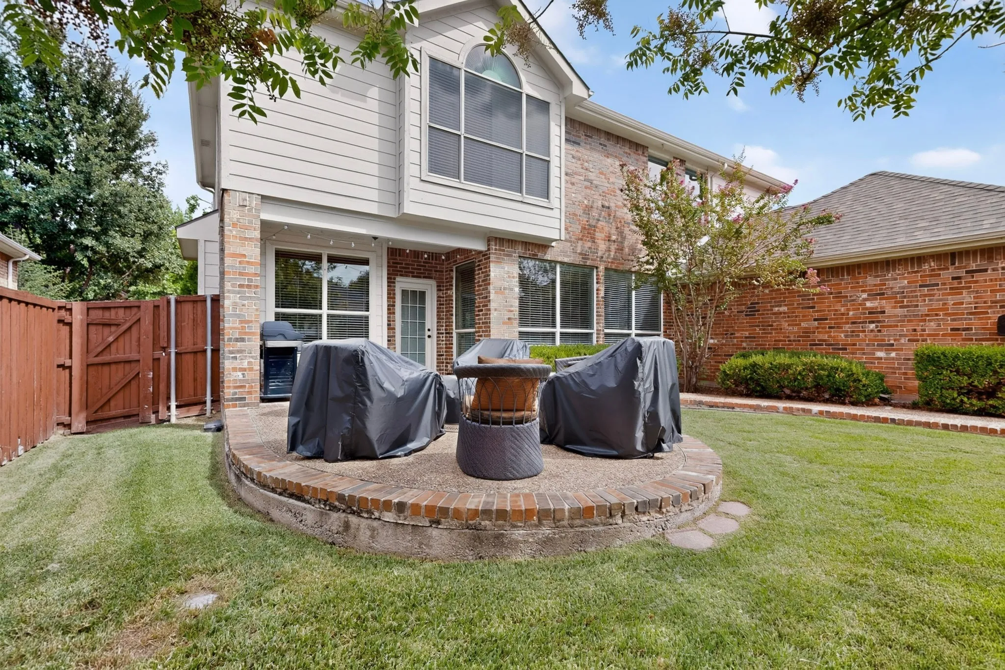 Brick and siding exterior featuring an elevated paver patio, wood fencing, and a glass-paneled door