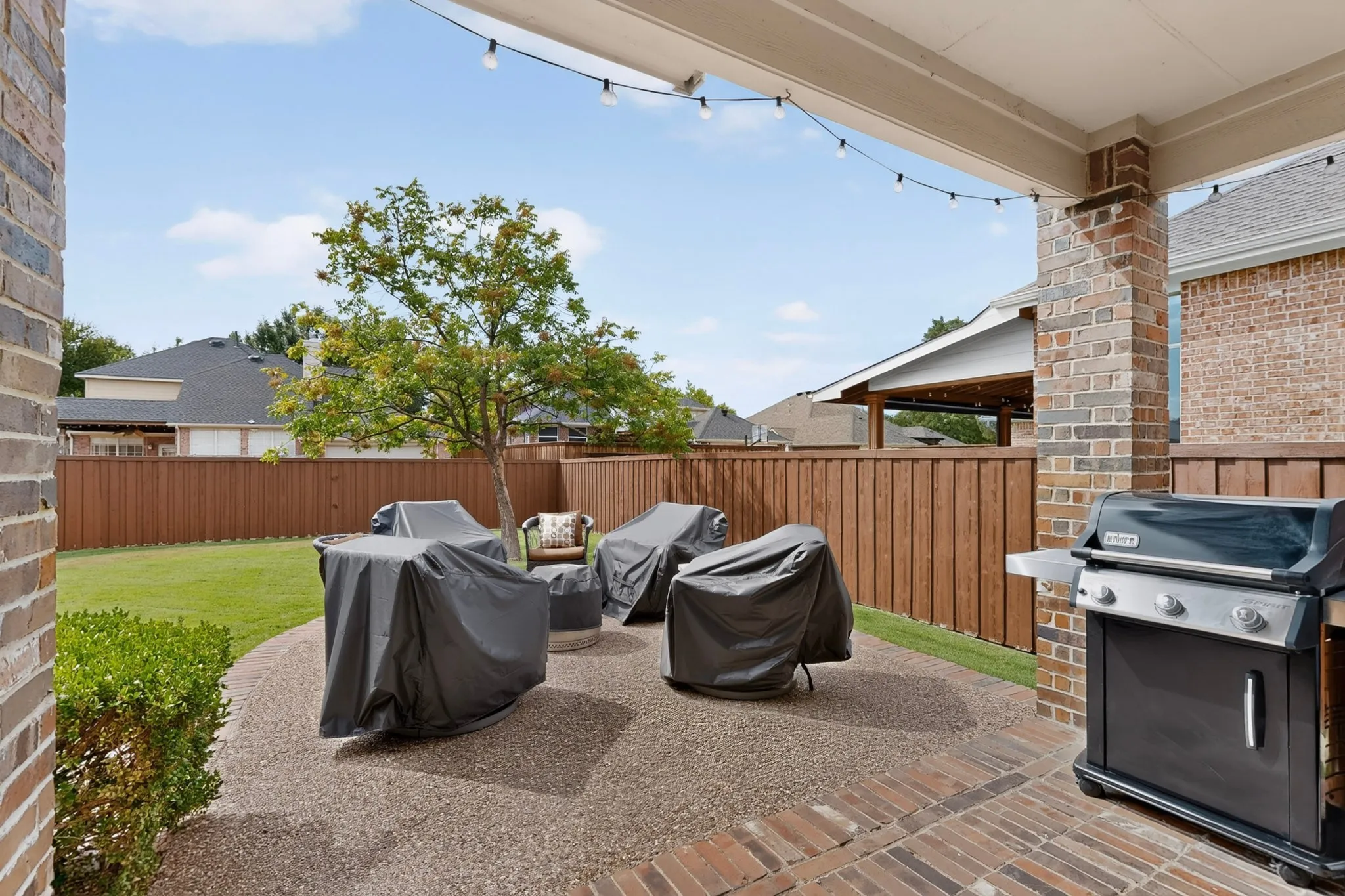 Expansive backyard featuring a manicured lawn, wood fencing, and a brick patio with an exposed aggregate extension
