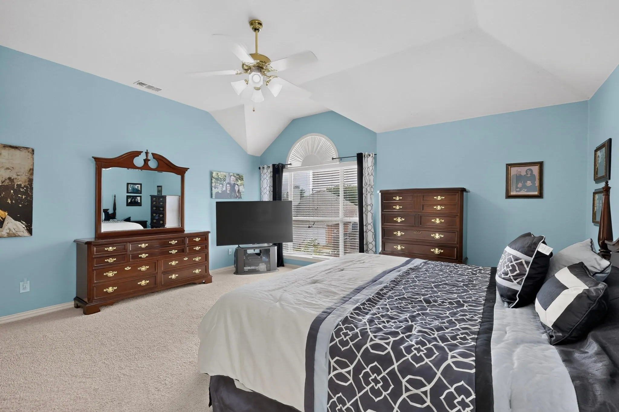 Vaulted ceiling with a ceiling fan, arched window with blinds, and light-colored carpeting