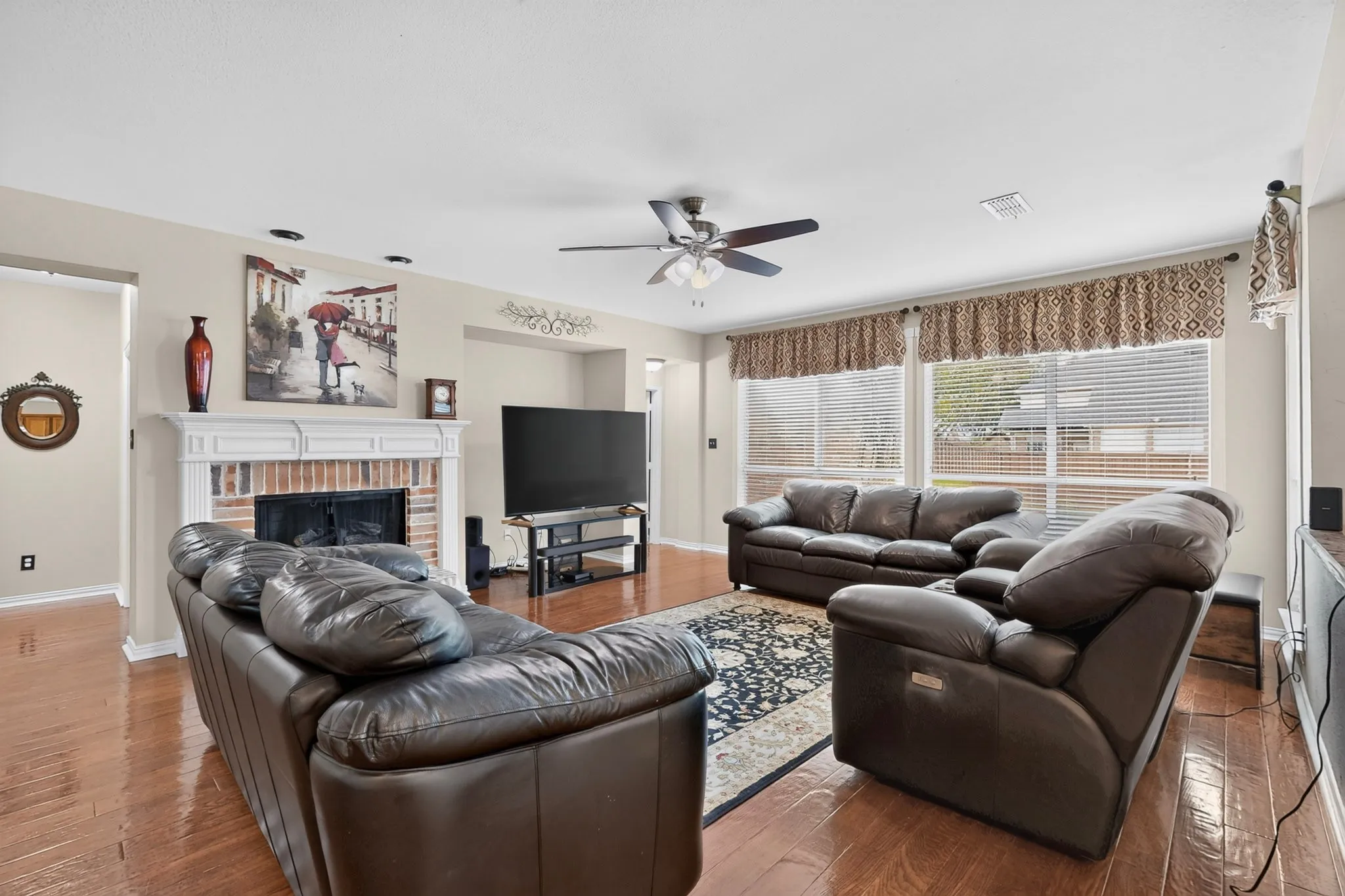 Expansive living area featuring wood-finish flooring, a ceiling fan, and a brick fireplace with a white mantel