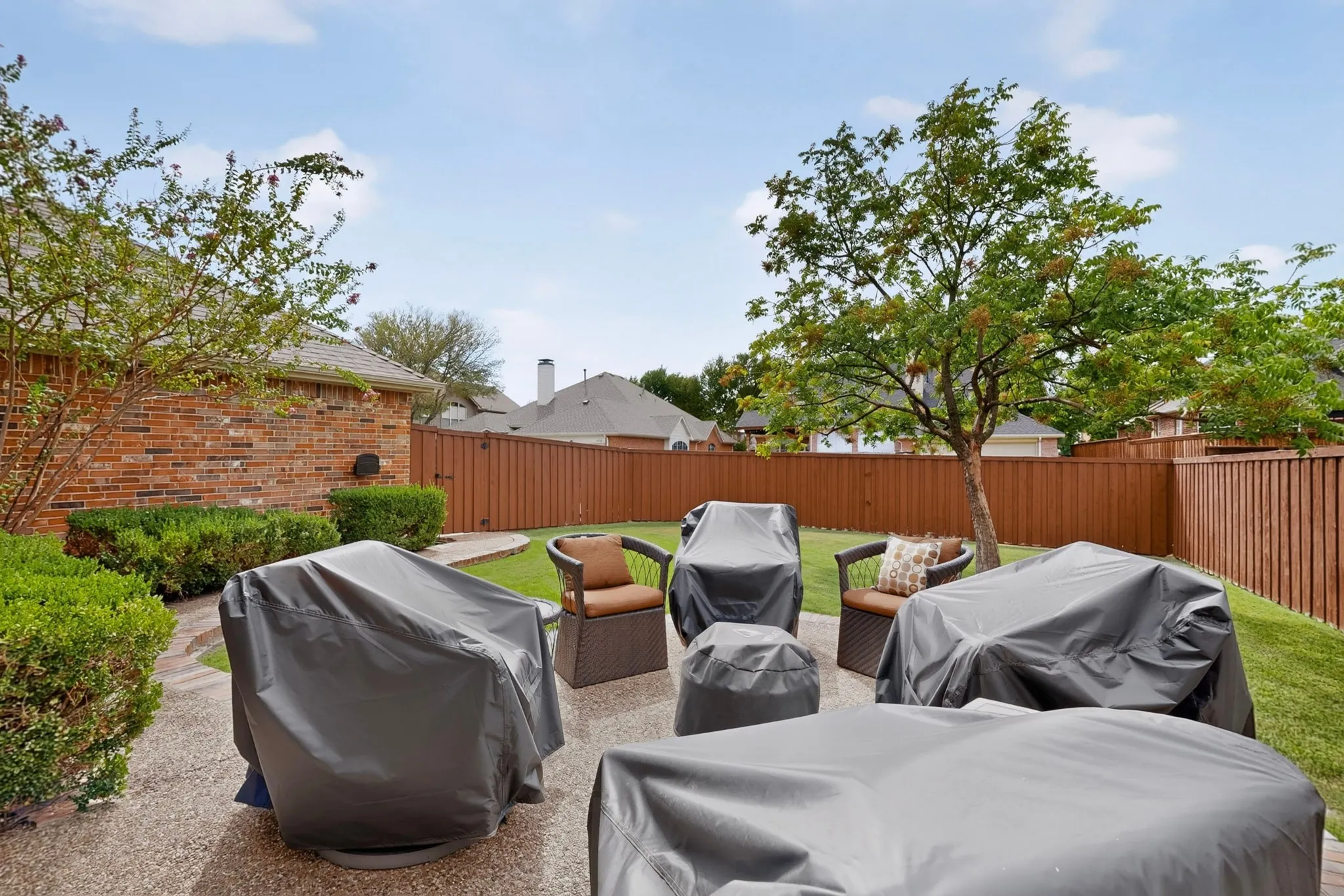 Expansive backyard featuring a red brick exterior, a wood privacy fence, green lawn, and mature trees