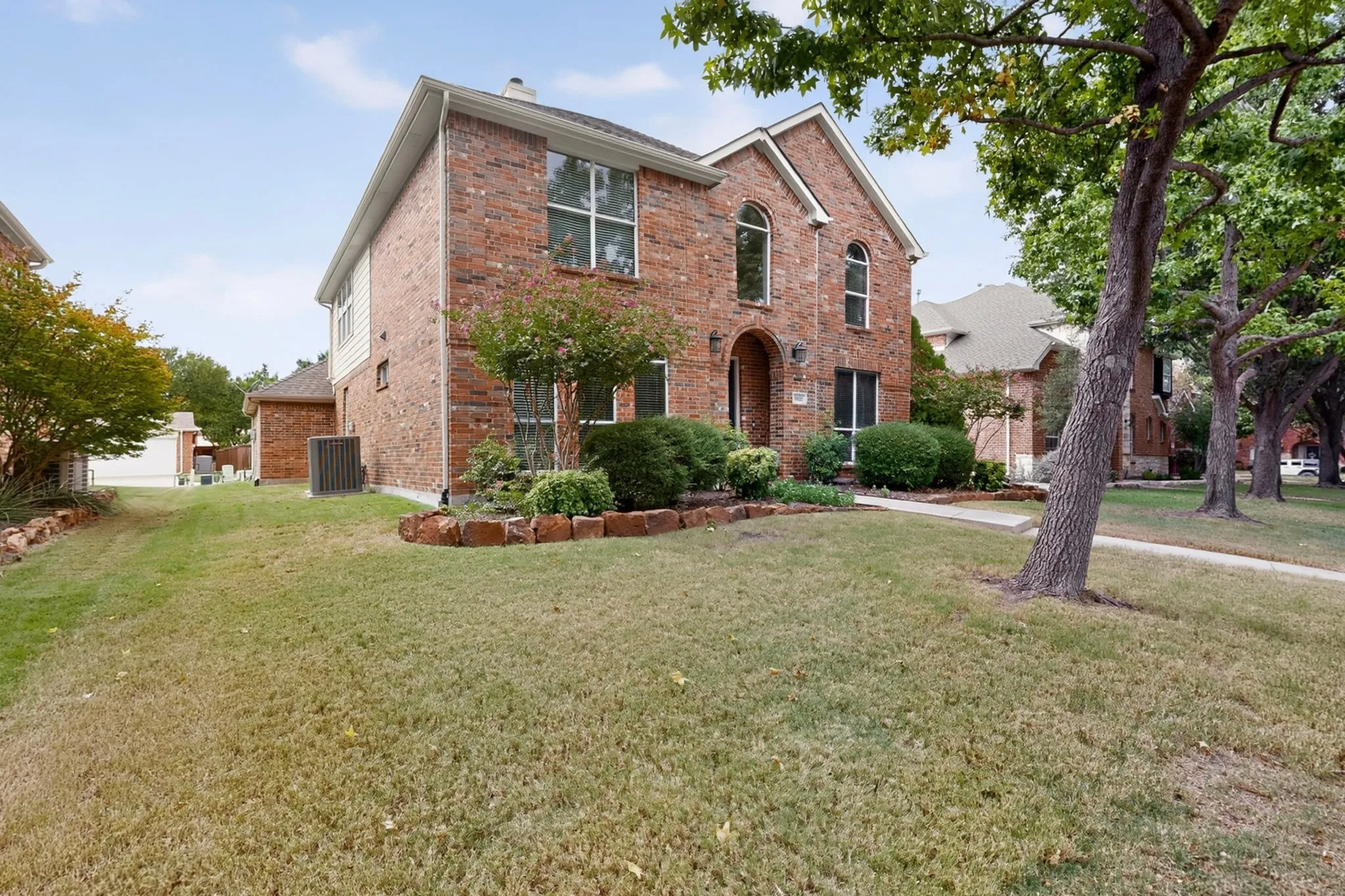 Brick exterior, arched window accents, mature trees, established landscaping, and a concrete walkway