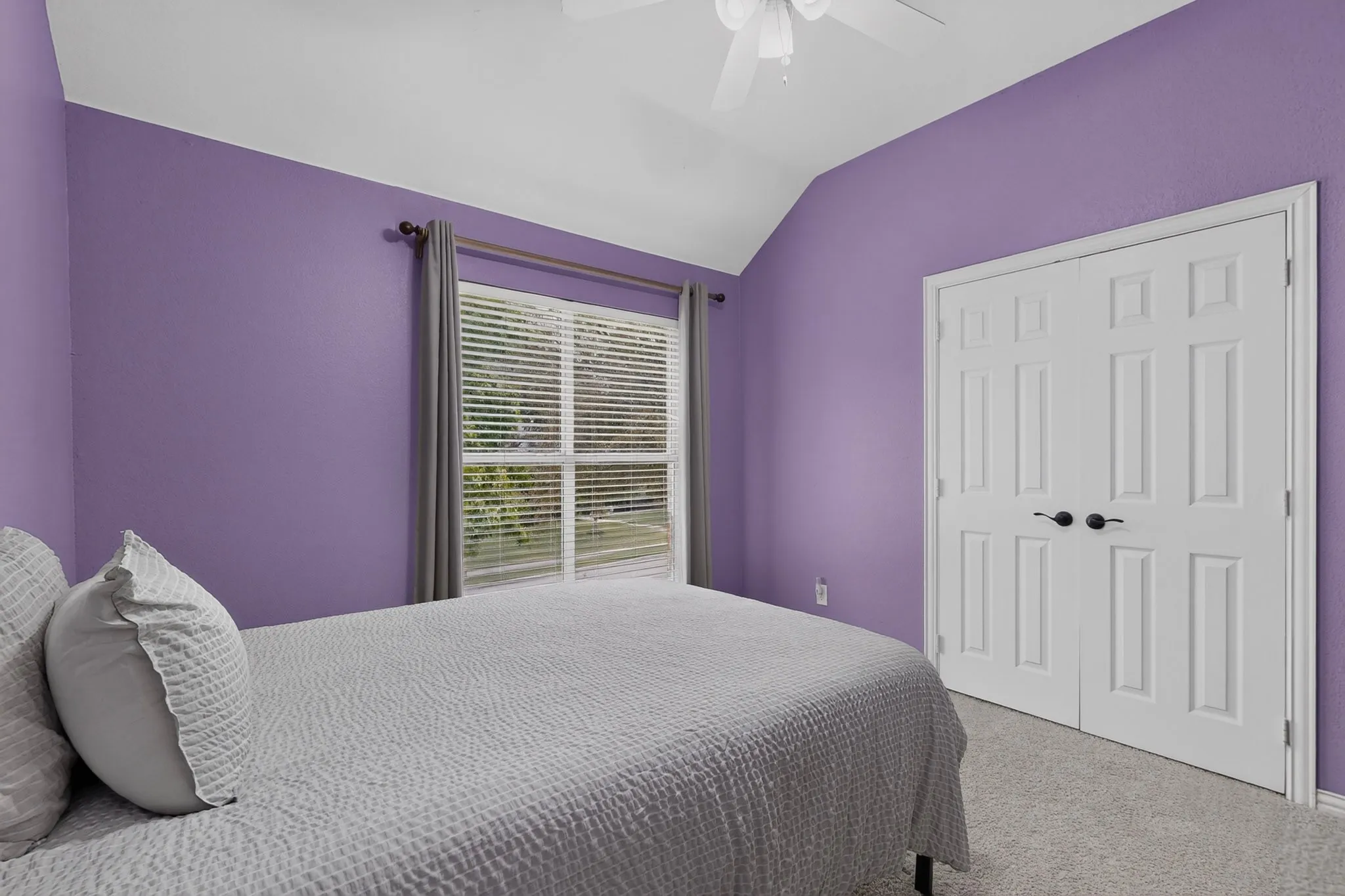 Vaulted ceiling featuring a ceiling fan, window with blinds and curtains, and bi-fold paneled doors