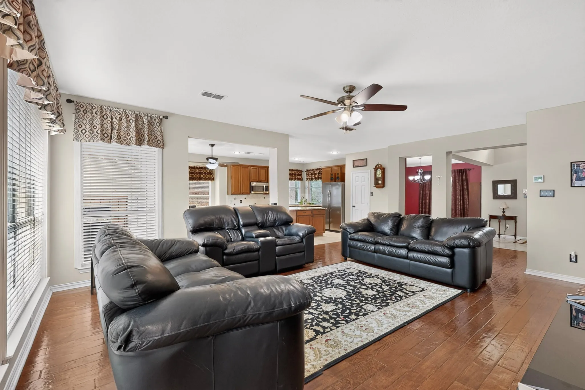 Expansive living area with wood-finish flooring, two large windows, and a ceiling fan