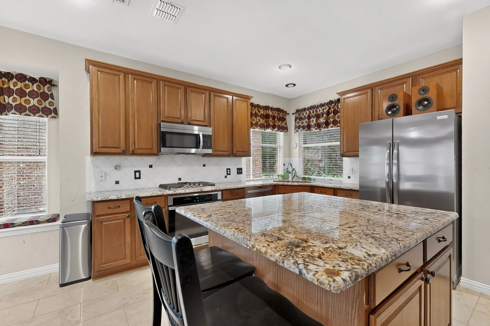 Kitchen featuring wood cabinetry, stainless steel appliances, a stone countertop island, and tile flooring