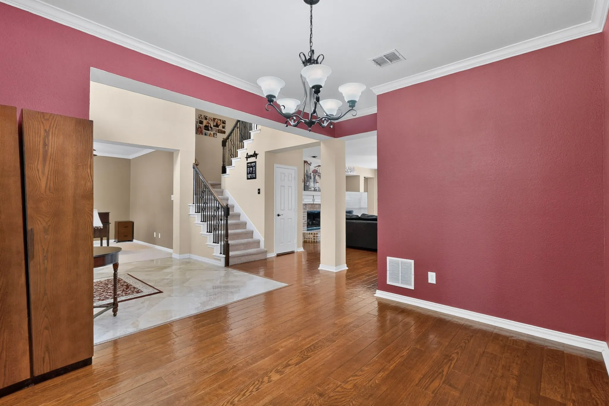 Hardwood flooring, crown molding, chandelier lighting, staircase with wrought iron balusters, and tile flooring with decorative inlay