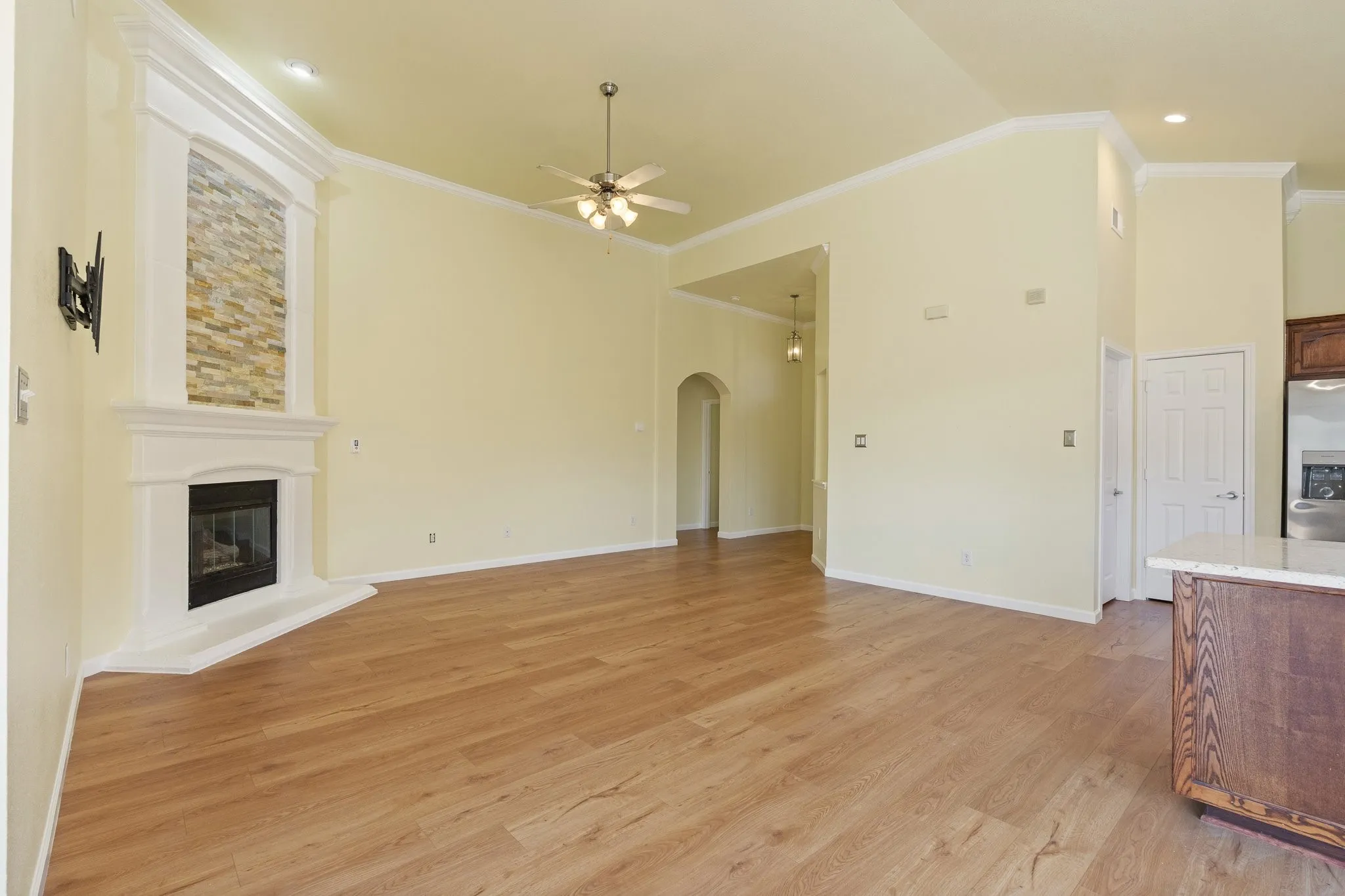 Spacious room featuring wood-finish flooring, a contemporary fireplace with stacked stone surround, ceiling fan, and crown molding