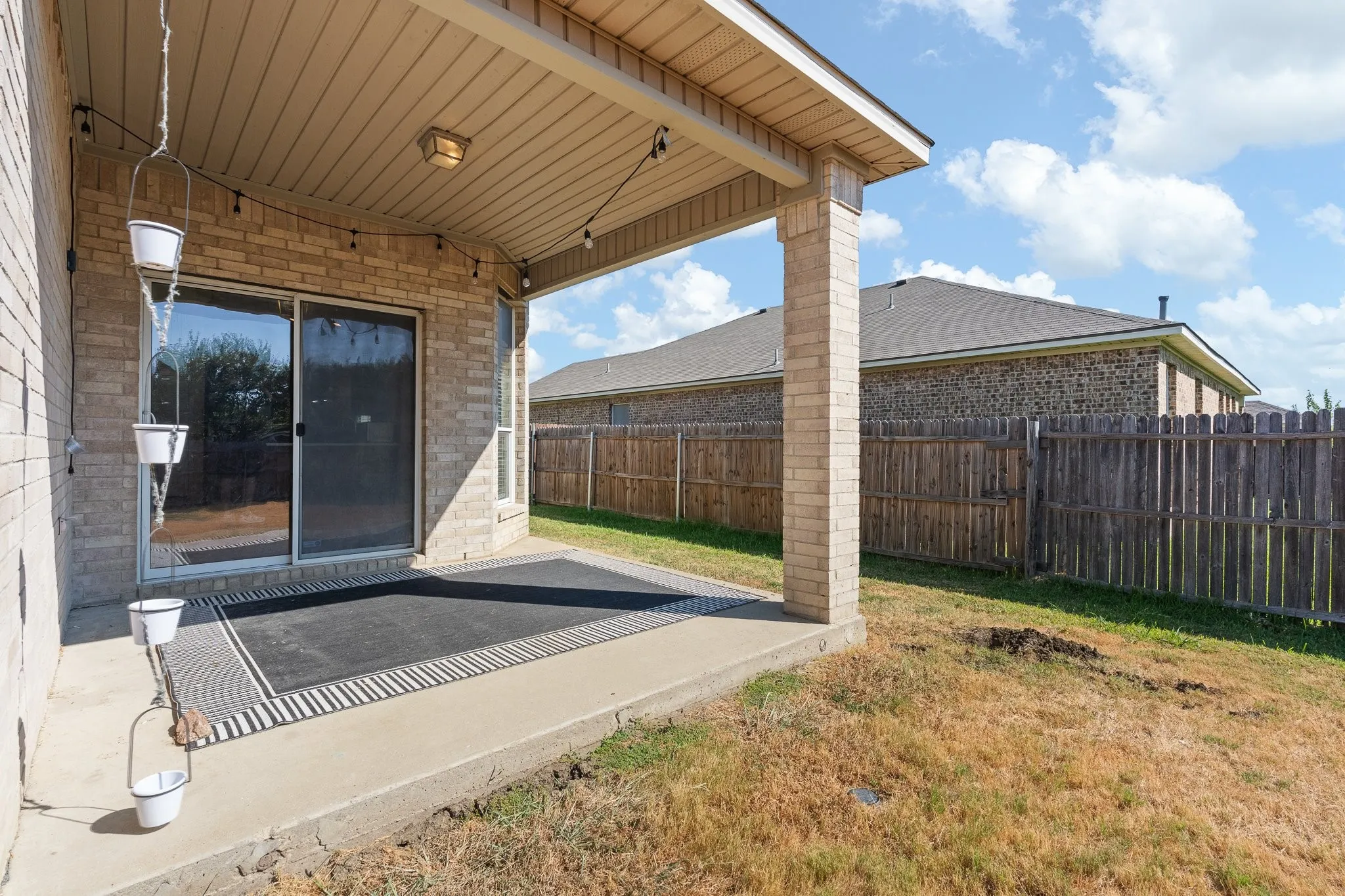 Covered patio with a brick column, brick exterior, and sliding glass door