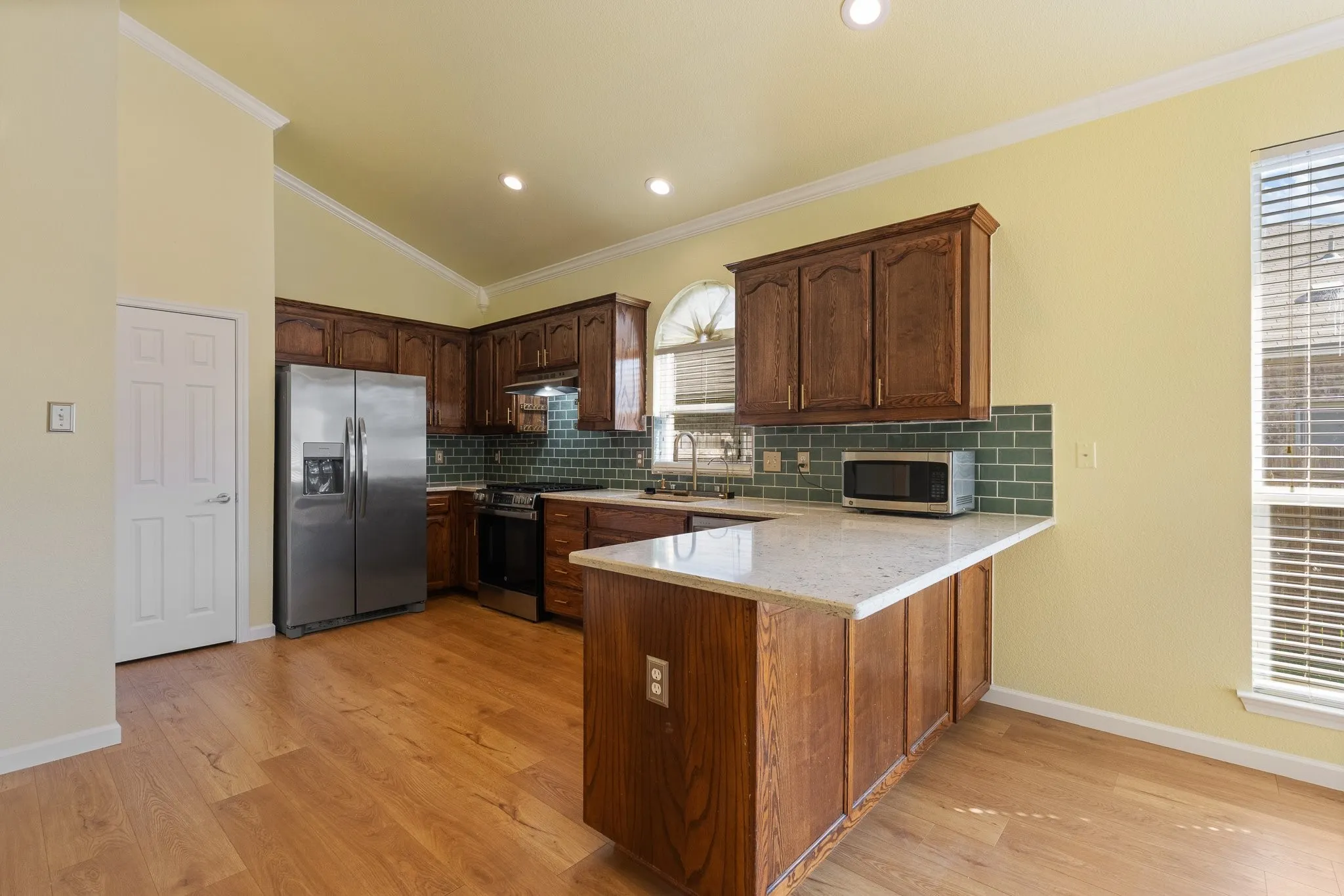 Kitchen featuring wood-finish flooring, vaulted ceilings, recessed lighting, and wood cabinetry with stainless steel appliances