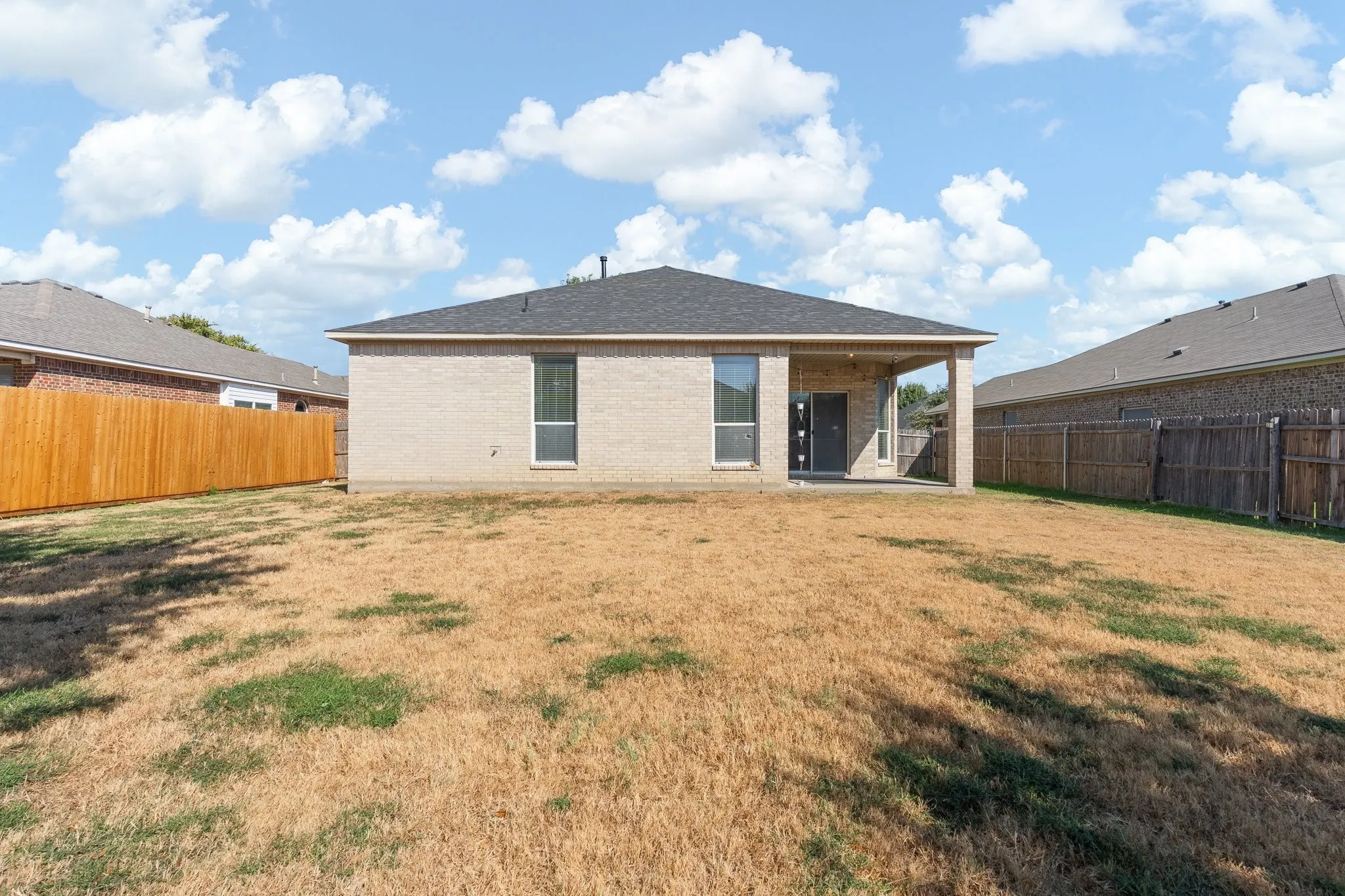 Rear exterior with a covered patio, brick facade, and a dark shingle roof