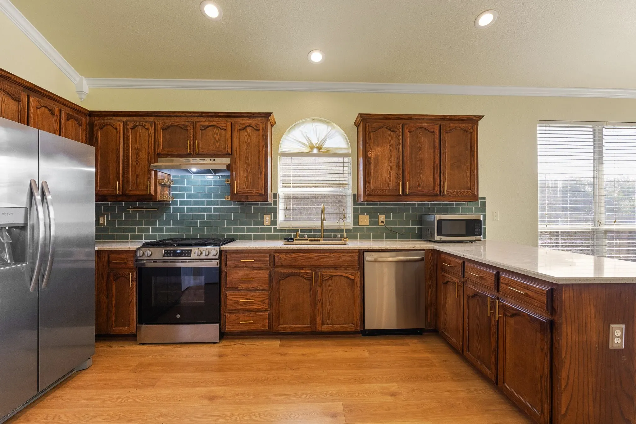 Wood-finish flooring with recessed lighting, crown molding, and a tiled backsplash