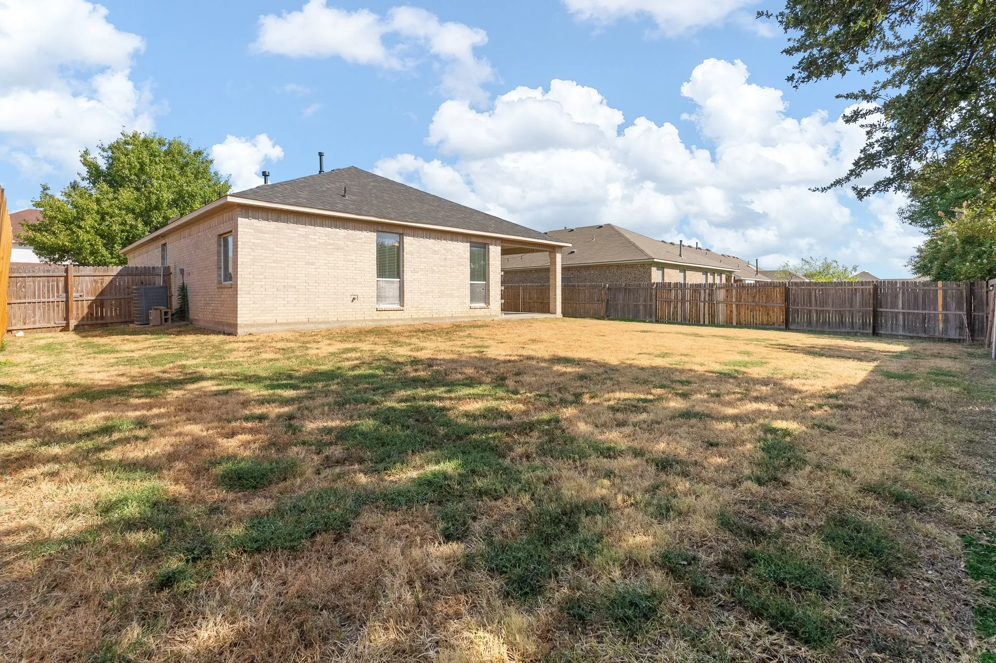 Expansive backyard featuring a wood fence, a covered patio, and a brick exterior